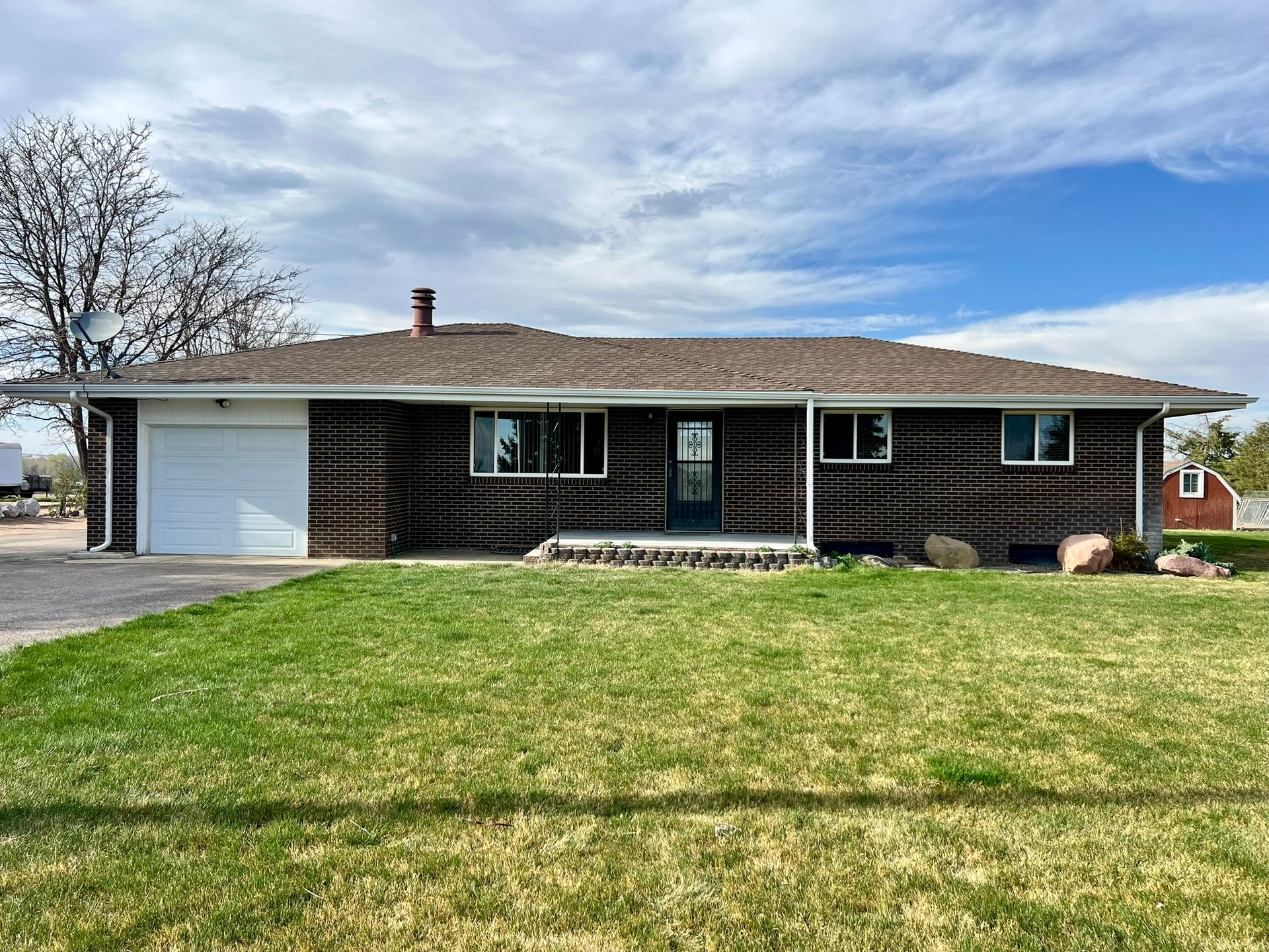 A brown house with a white garage door and a large lawn in front of it.