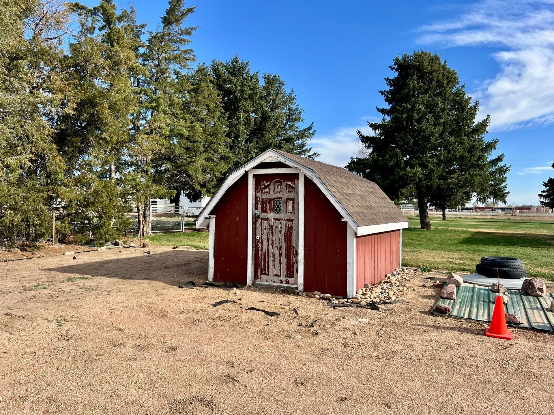 A small red barn is sitting in the middle of a dirt field.