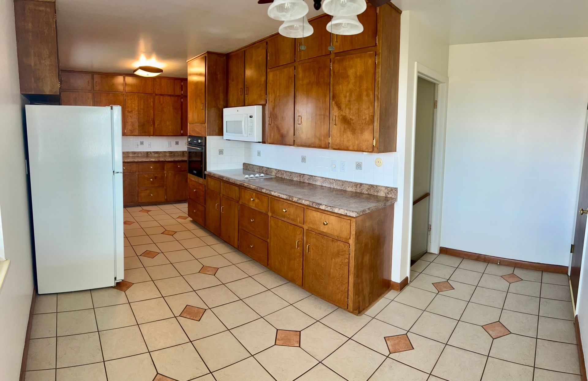 An empty kitchen with wooden cabinets and a white refrigerator