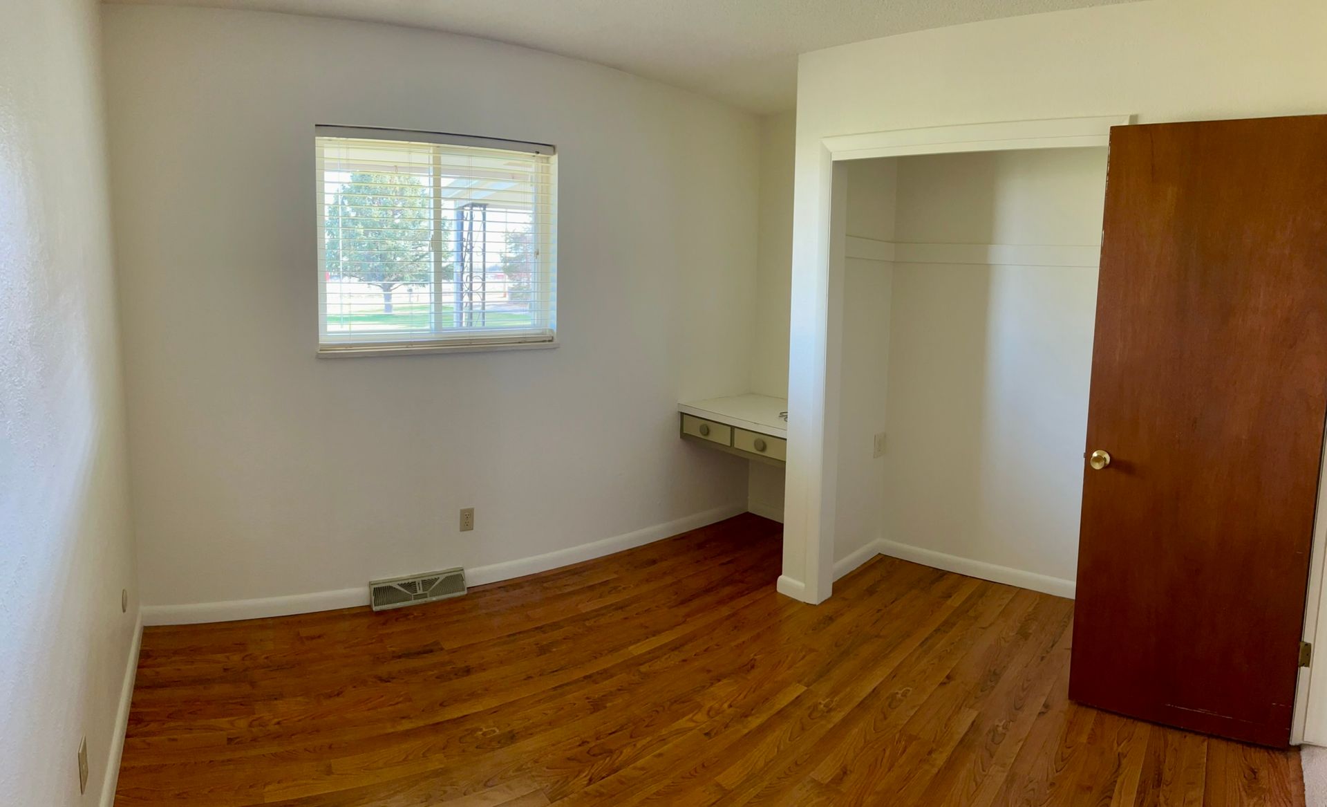 An empty bedroom with hardwood floors and a window.