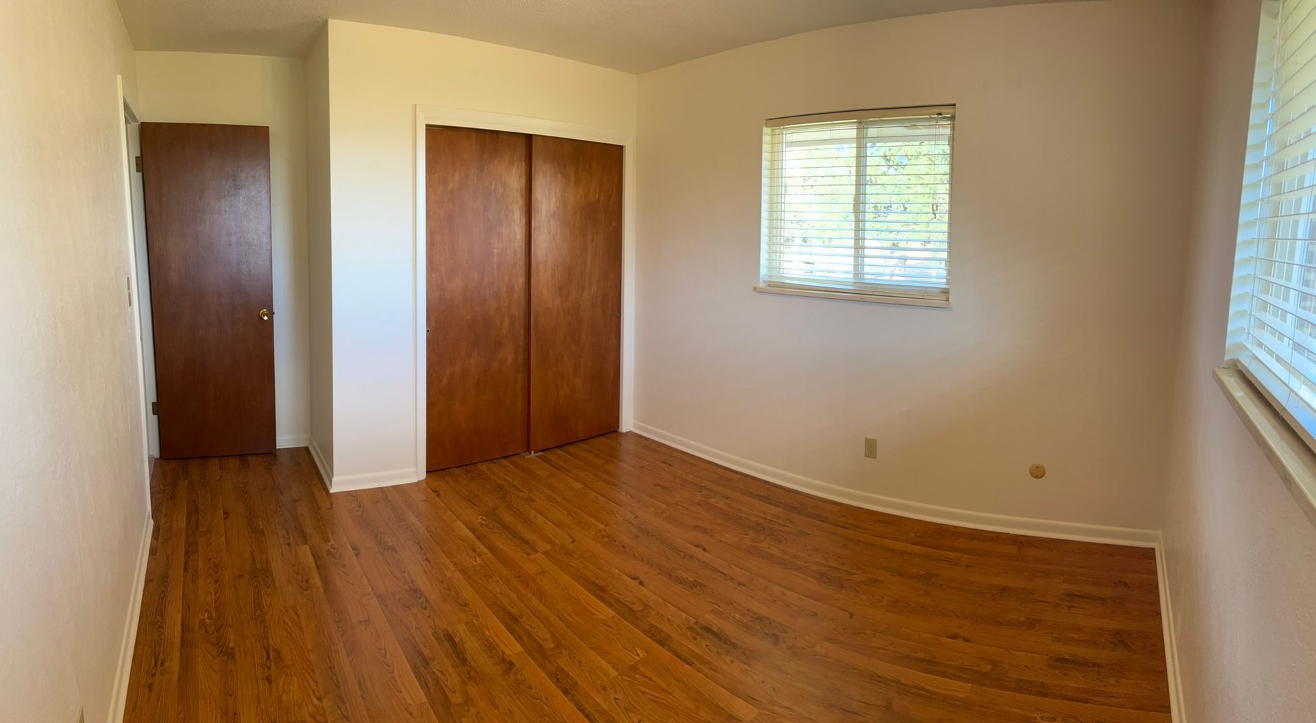 An empty bedroom with hardwood floors and a window.