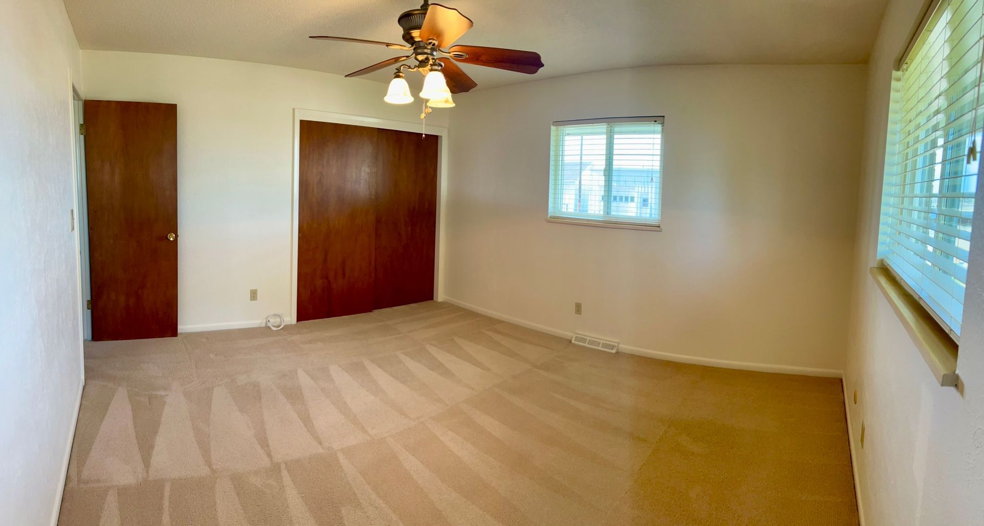 An empty room with a ceiling fan and a window.