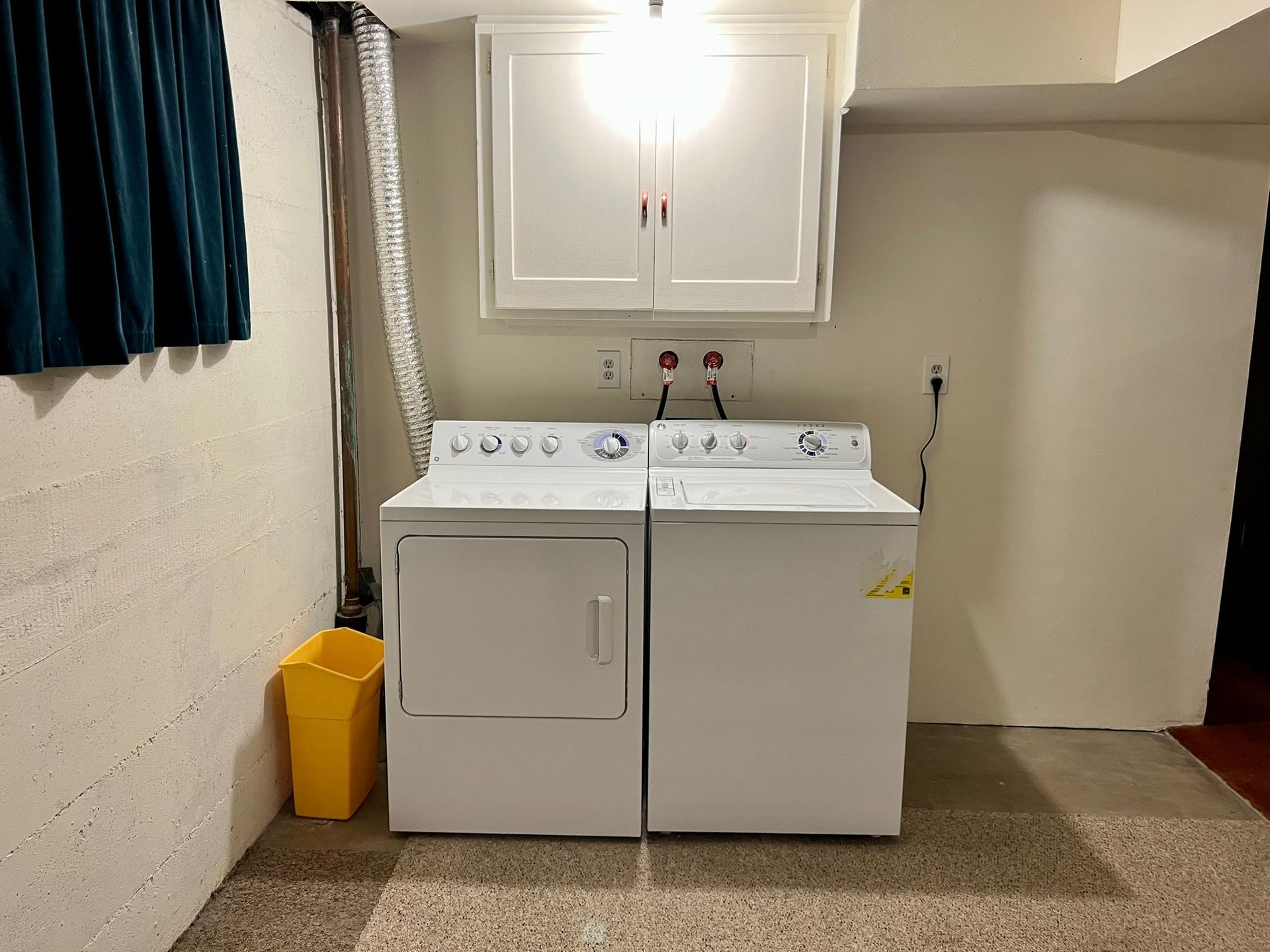 A laundry room with a washer and dryer and a yellow trash can.
