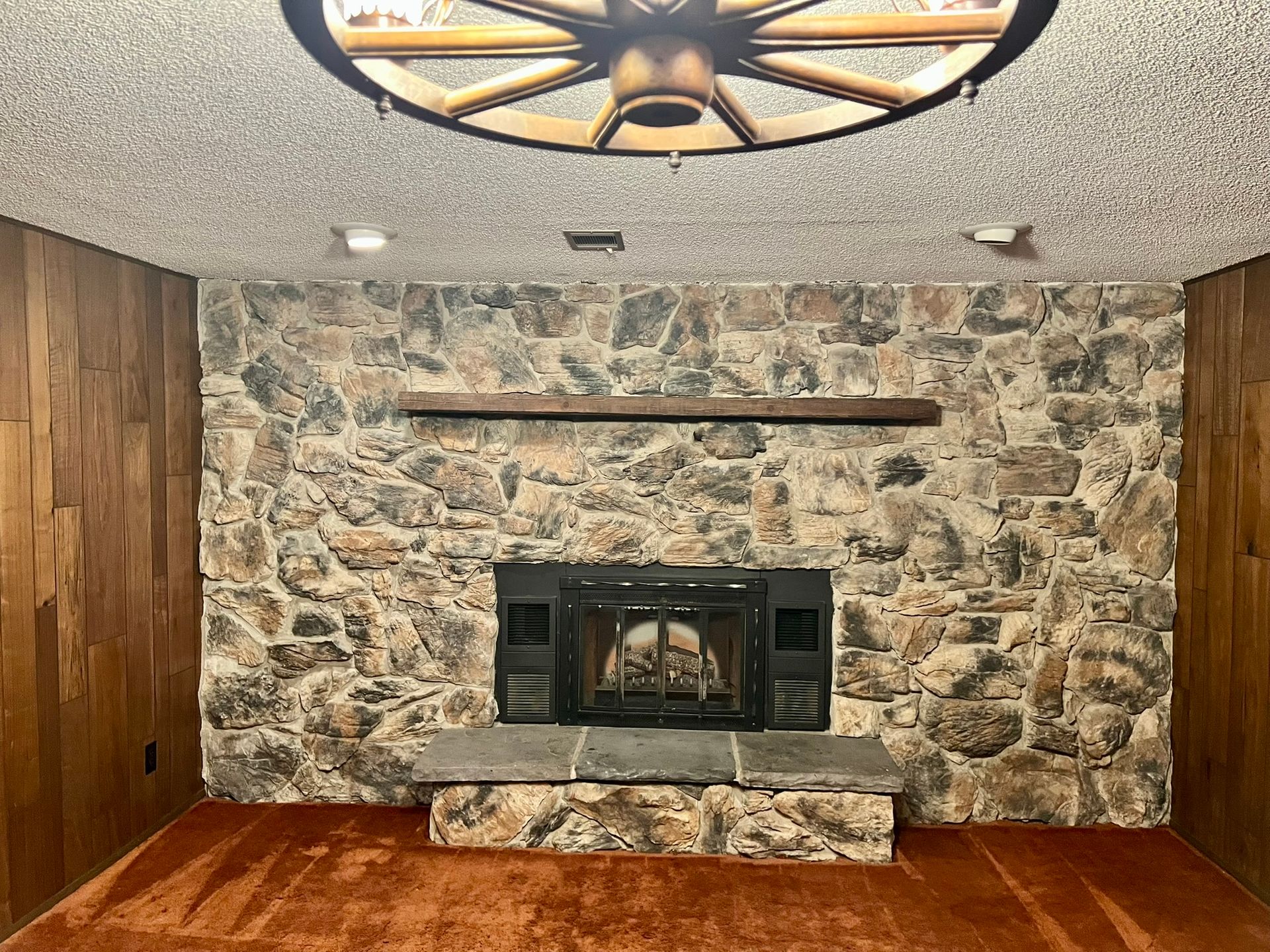 A living room with a fireplace and a wagon wheel on the ceiling.