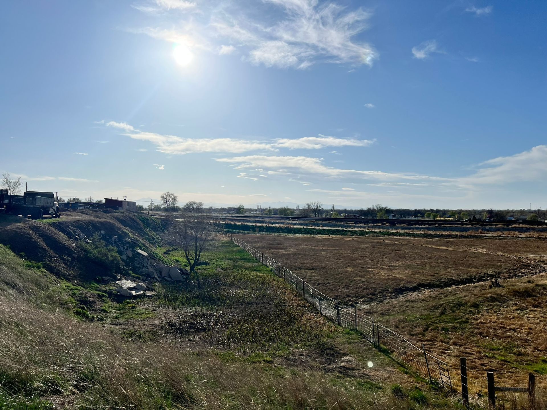 A large field with a fence in the foreground and a blue sky with clouds in the background.