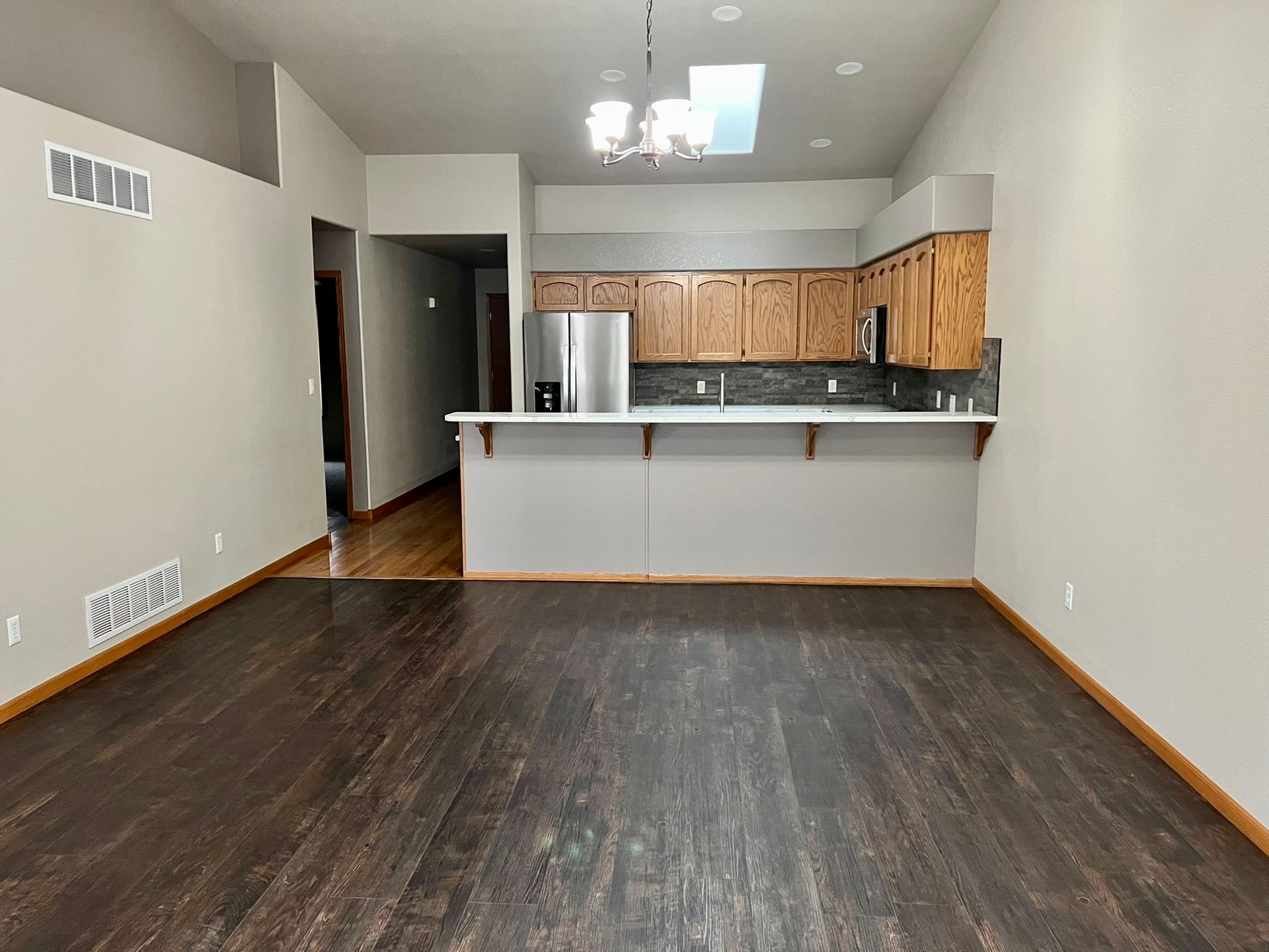 An empty living room with a kitchen in the background