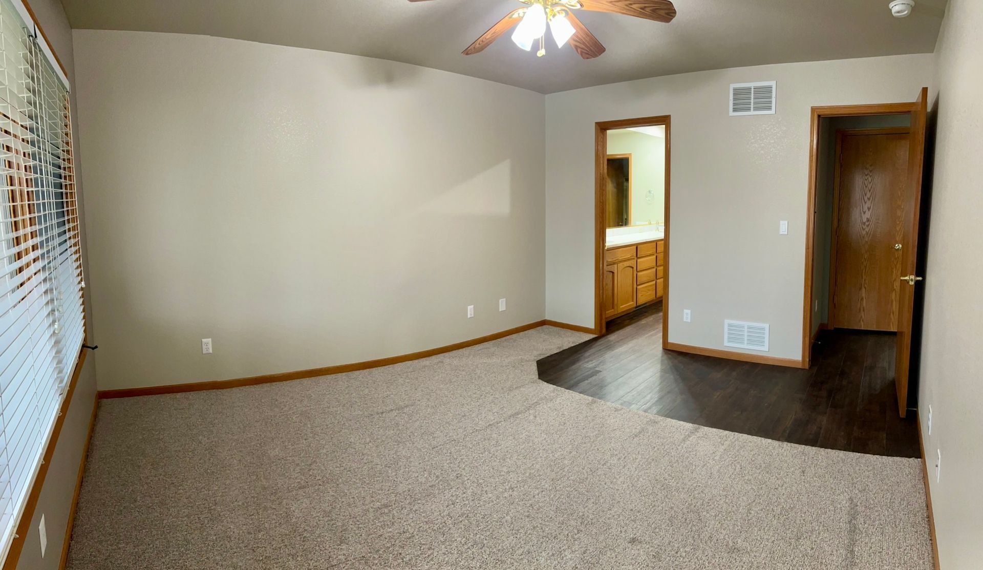 An empty living room with a ceiling fan and a window.
