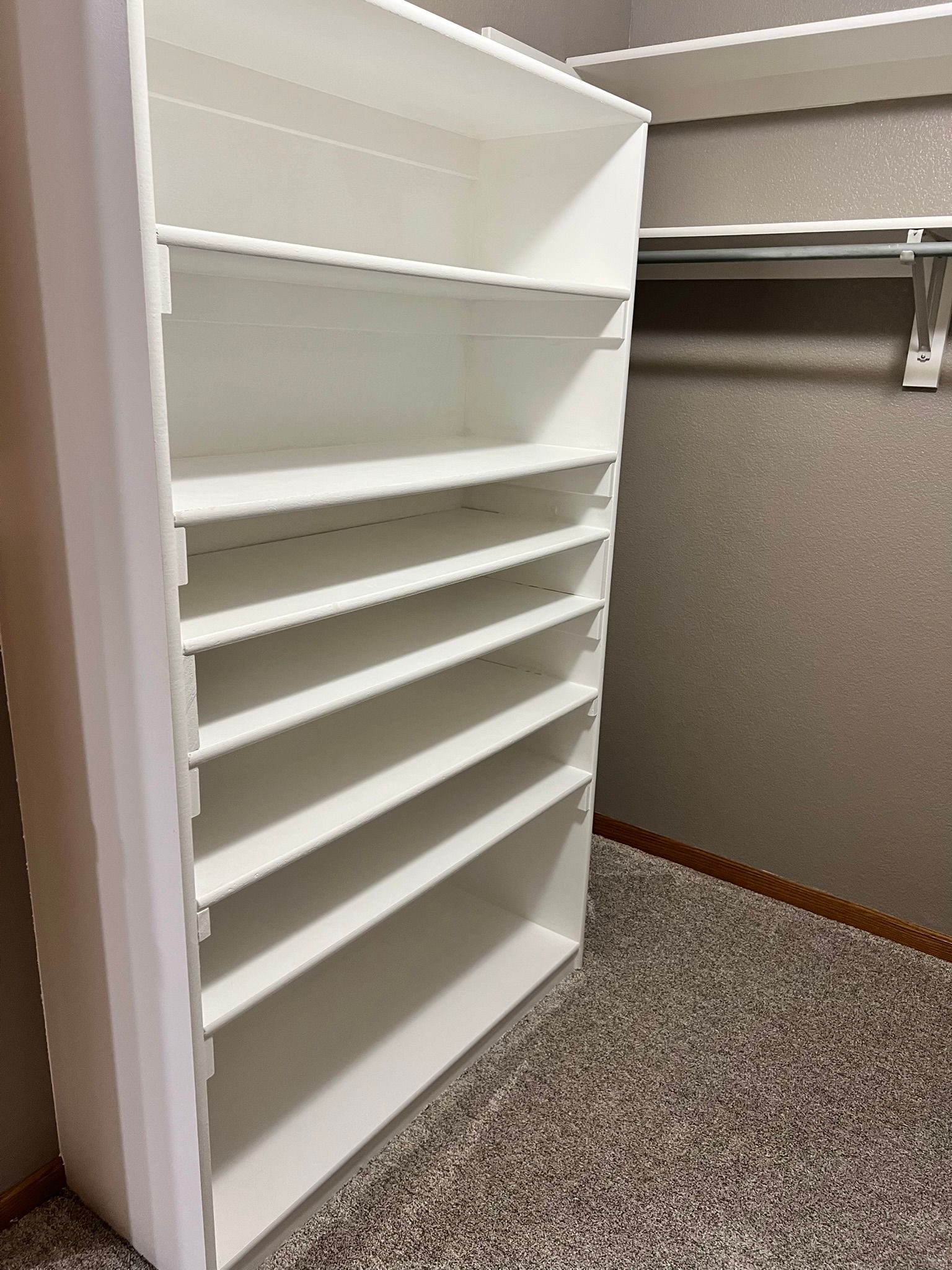 A walk in closet with a white shelf and a hanging rack.