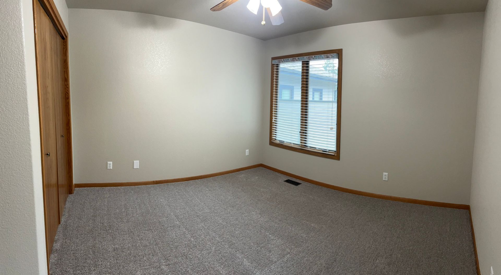 An empty bedroom with a ceiling fan and two windows.