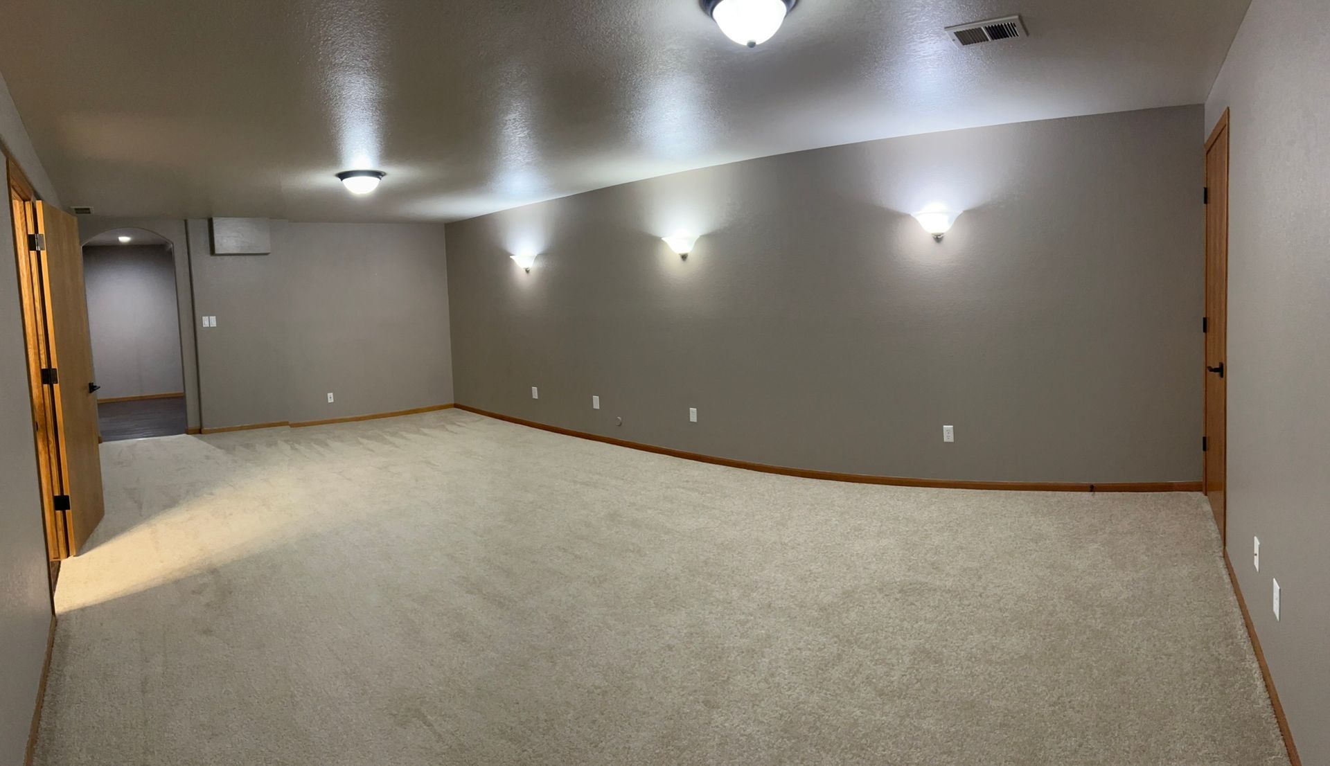 A large empty room with a carpeted floor and a ceiling fan.