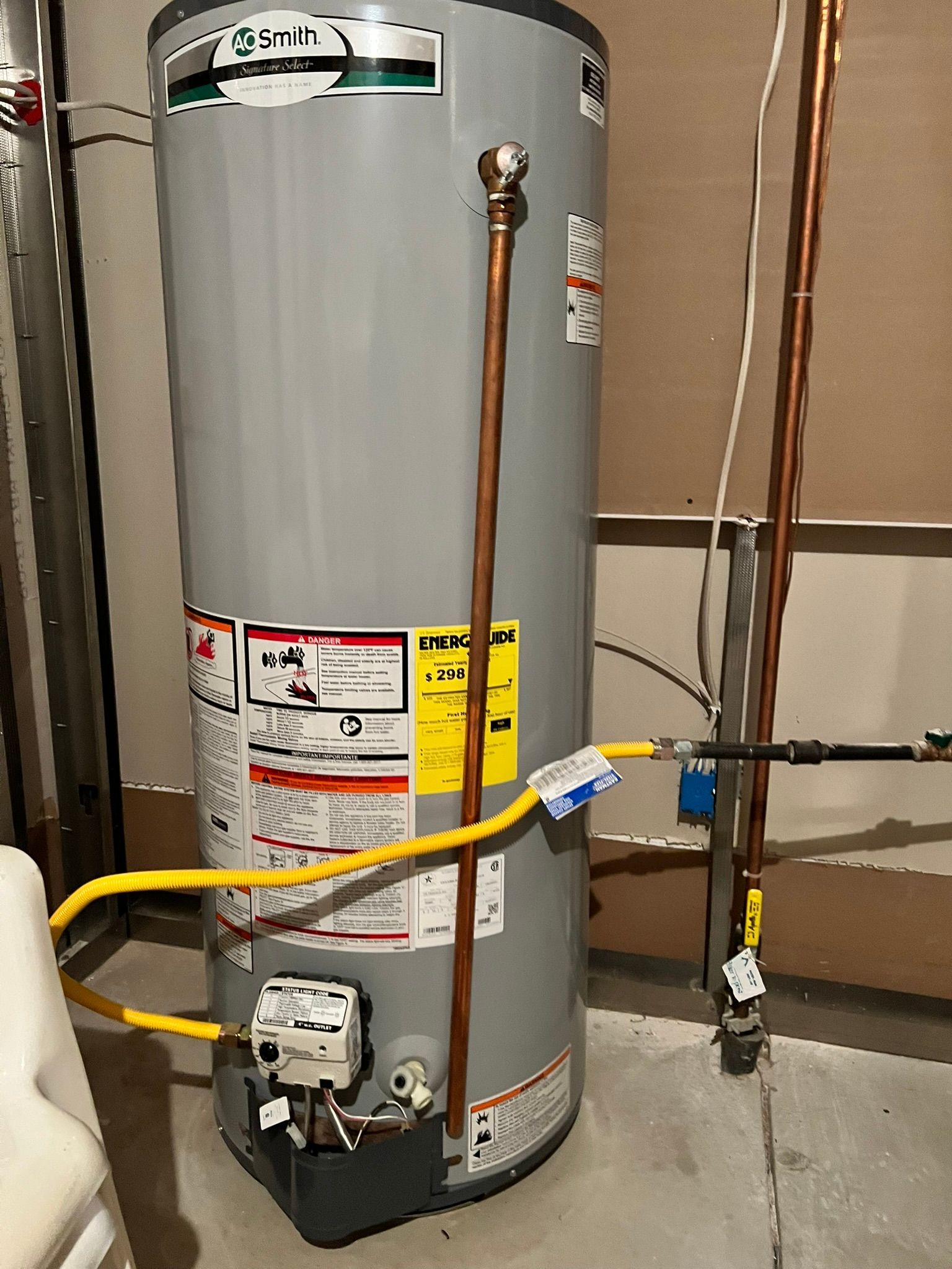 A gas water heater is sitting in a basement next to a wall.