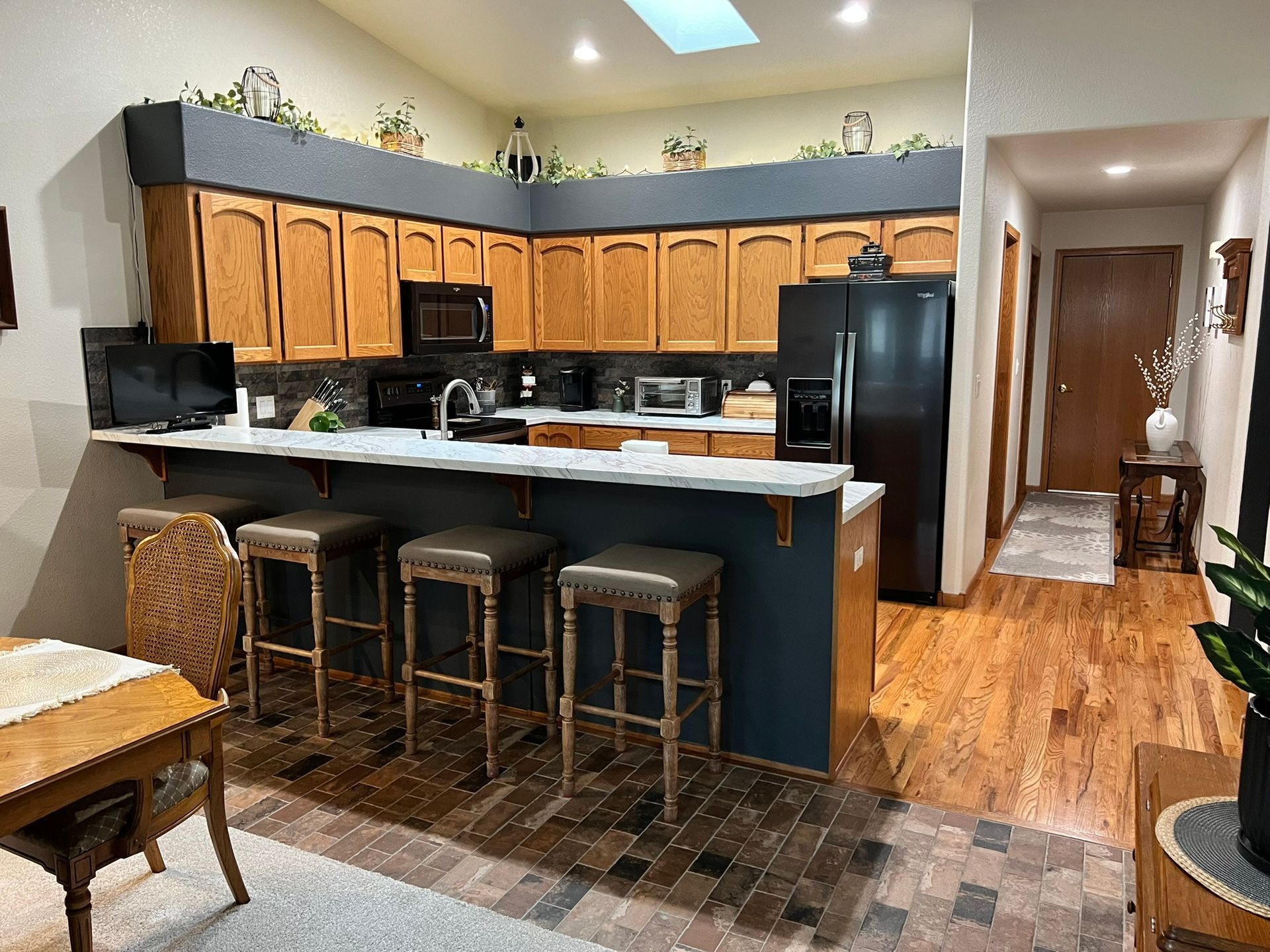 A kitchen with wooden cabinets , stools , a table and a refrigerator.