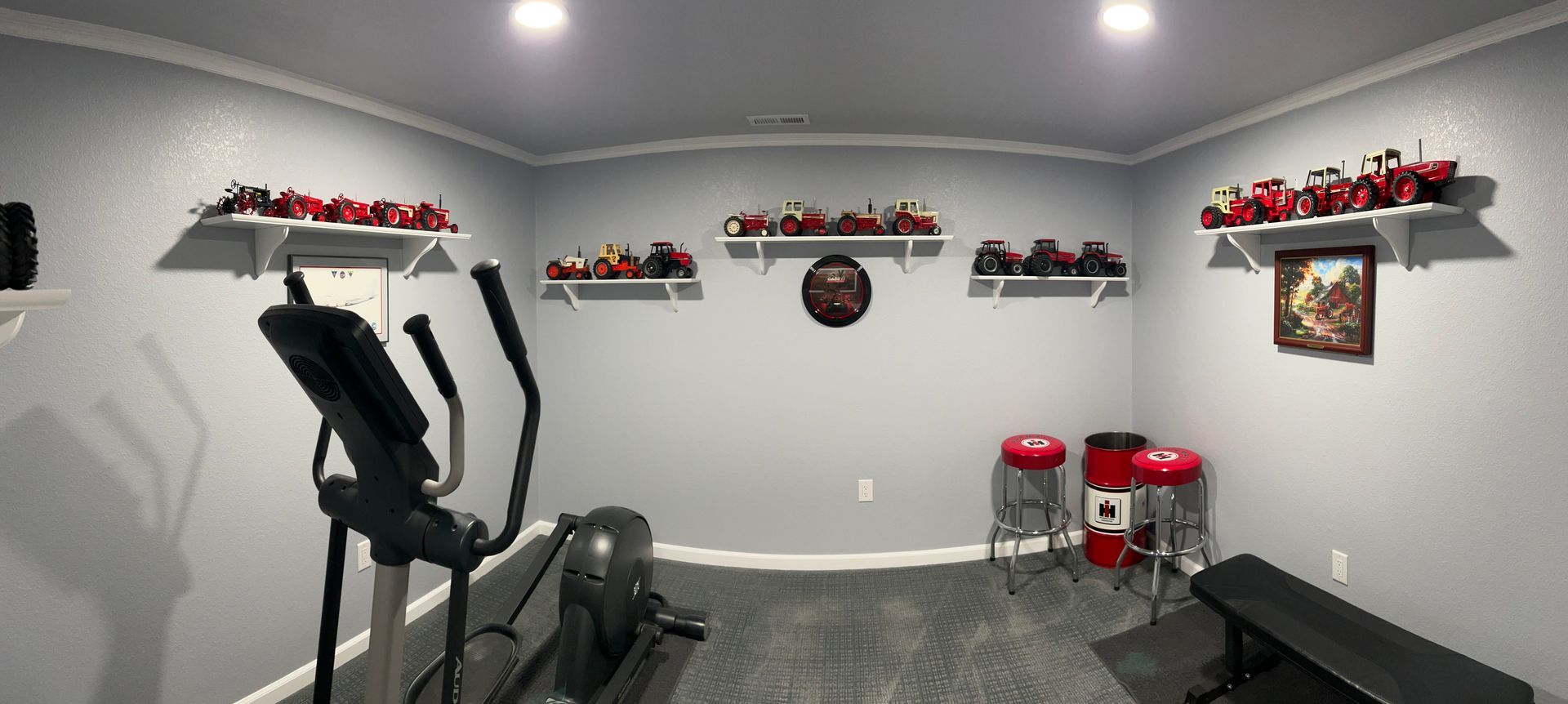 A home gym with a elliptical machine , bench , stools and a picture on the wall.
