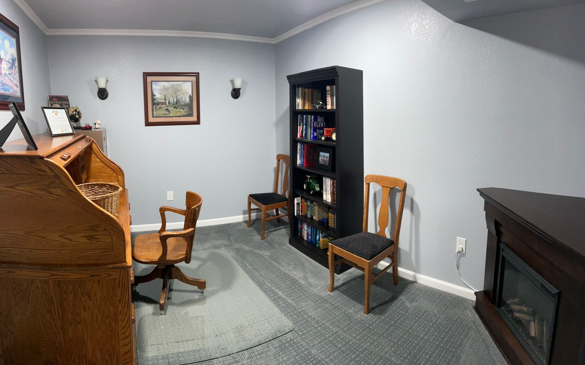 A room with a desk , chairs , a bookshelf and a fireplace.