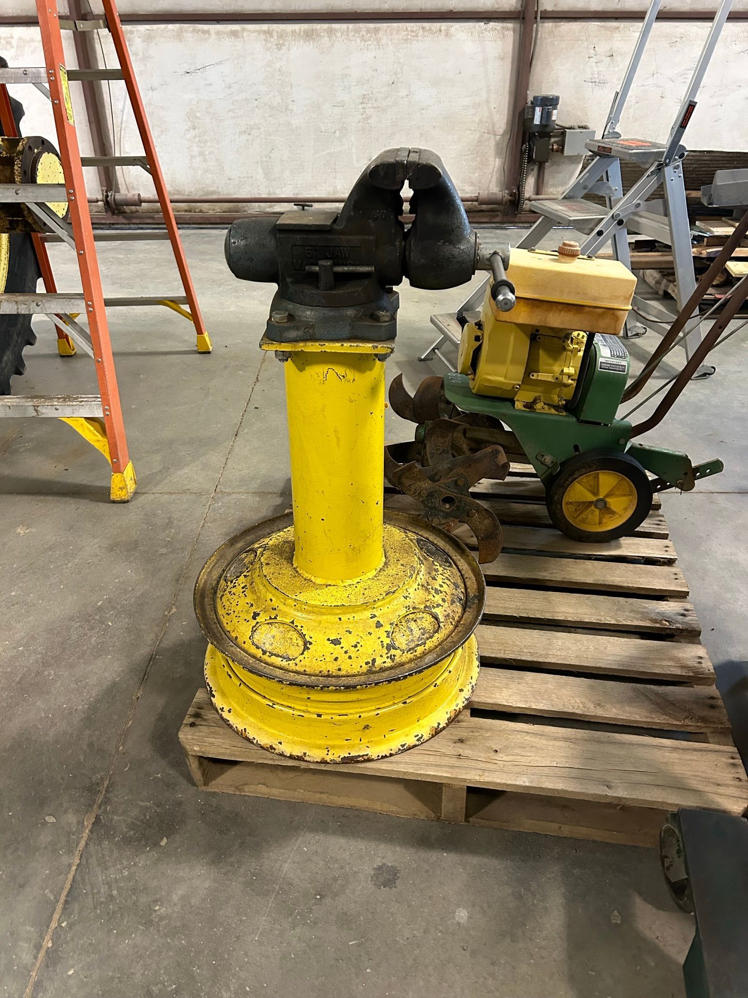 A yellow vise is sitting on top of a wooden pallet.