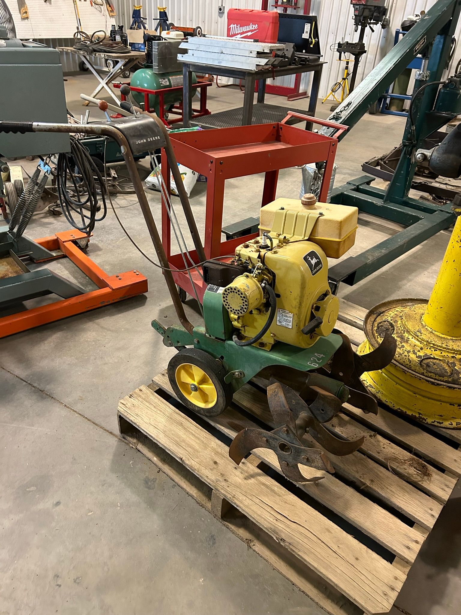 A small green and yellow lawn mower is sitting on top of a wooden pallet.