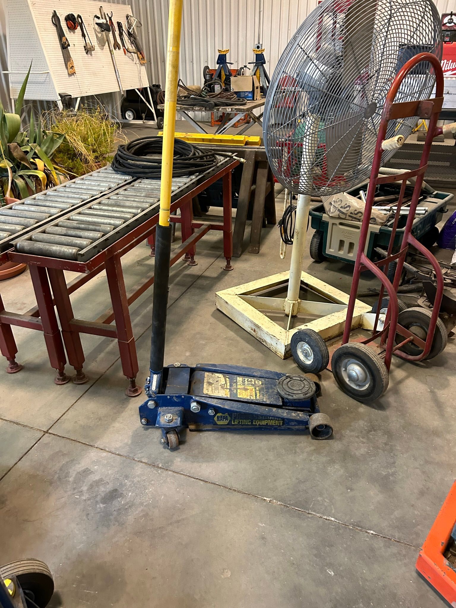 A blue jack is sitting on the floor in a garage next to a fan.