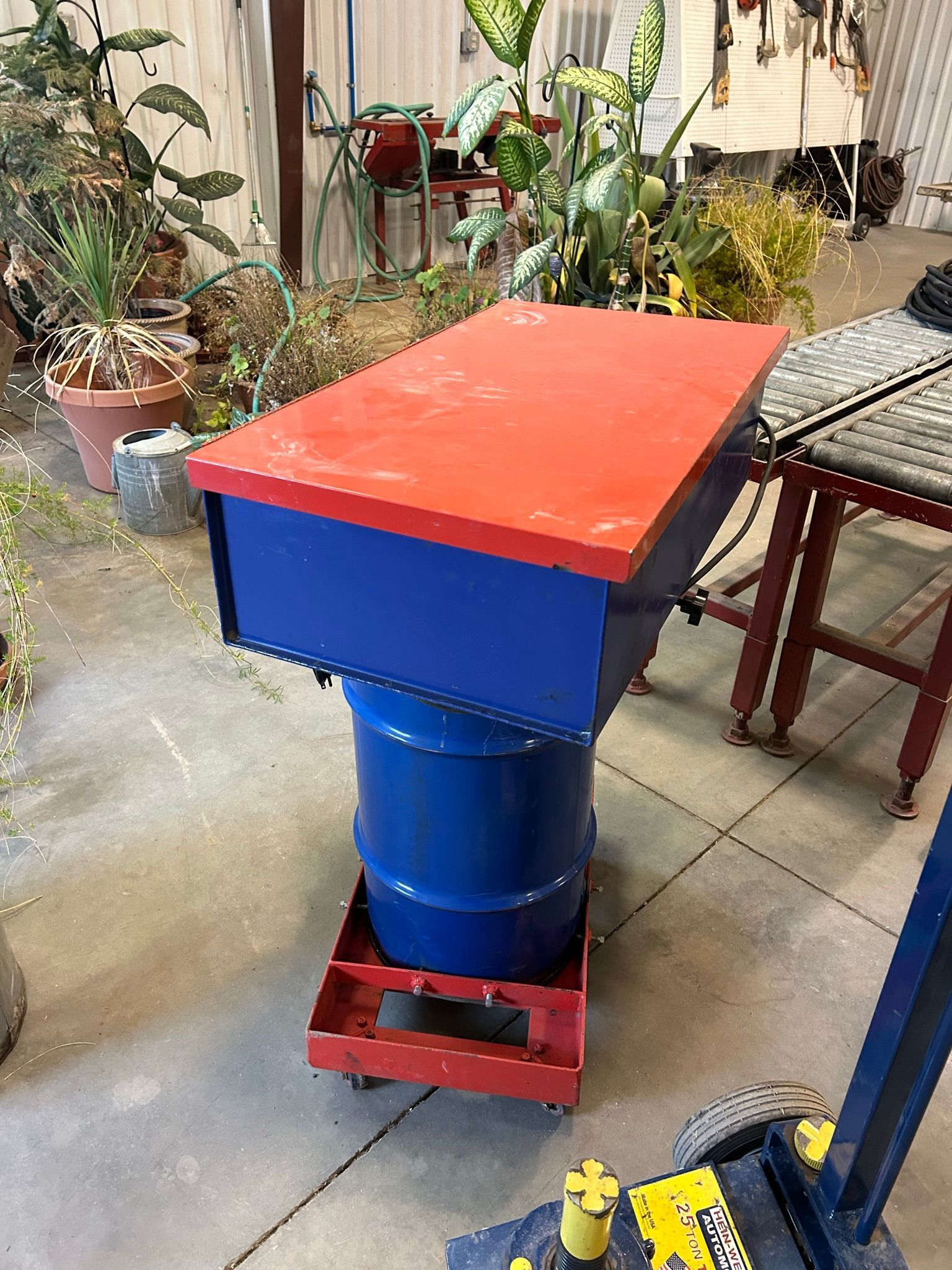 A blue barrel with a red top is sitting on a concrete floor.