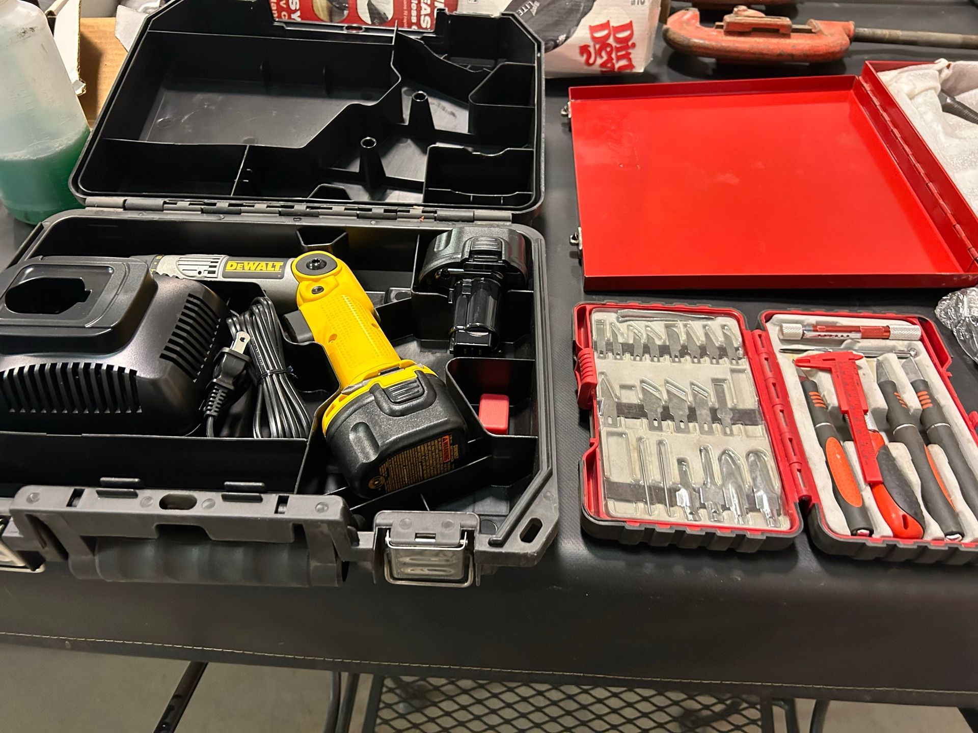 Black toolbox with yellow power drill, charger, and tool bits. Red tray and tool set on table.