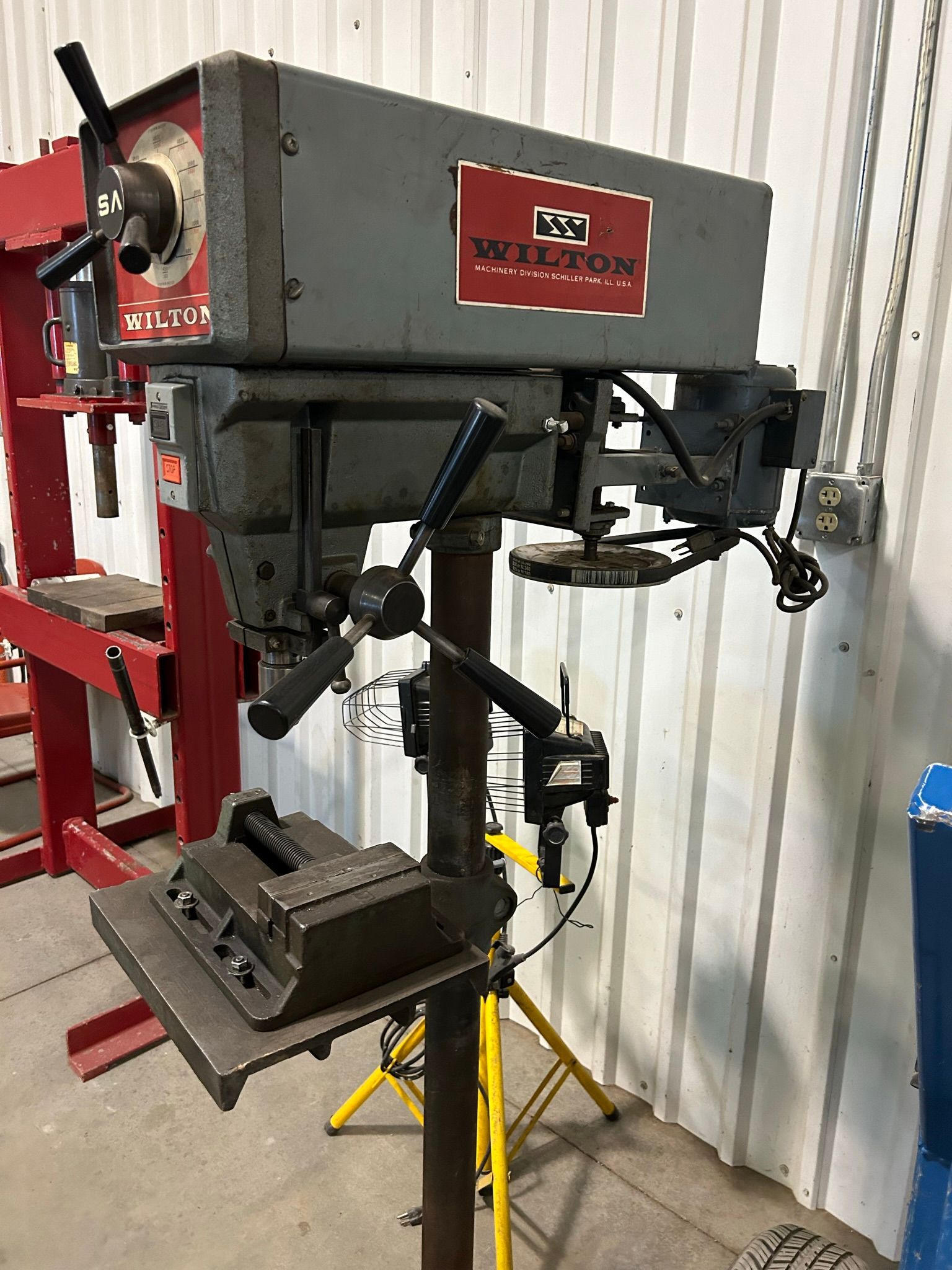 A drill press is sitting on top of a yellow stand in a garage.