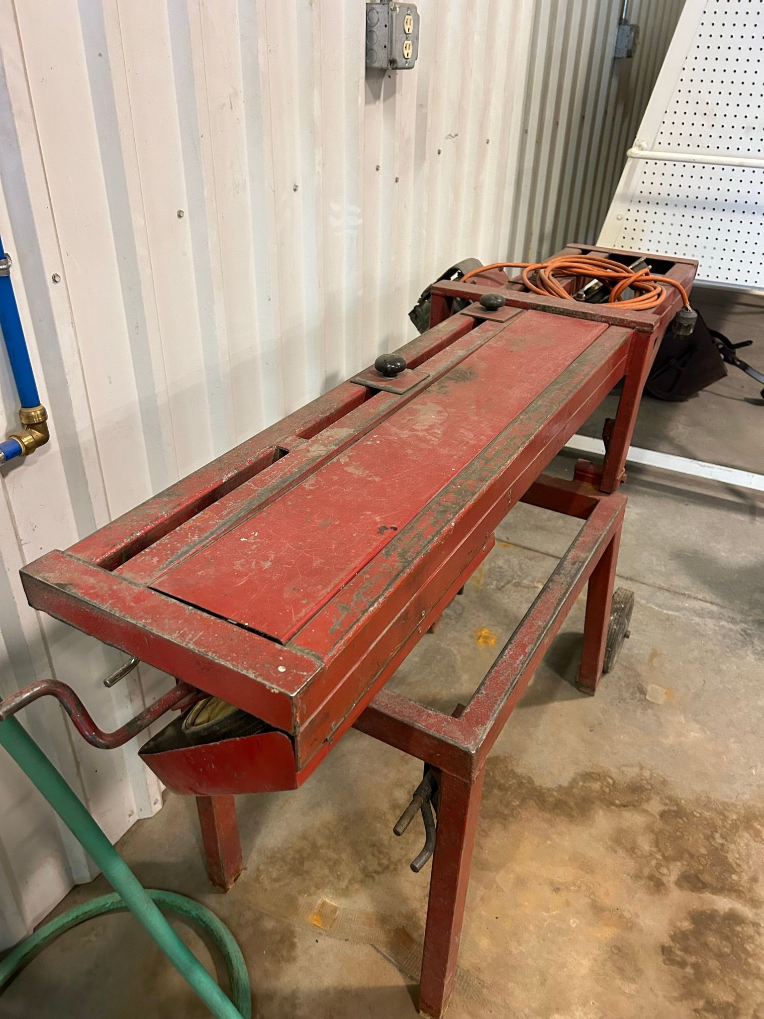 A red wooden workbench is sitting in a room next to a hose.