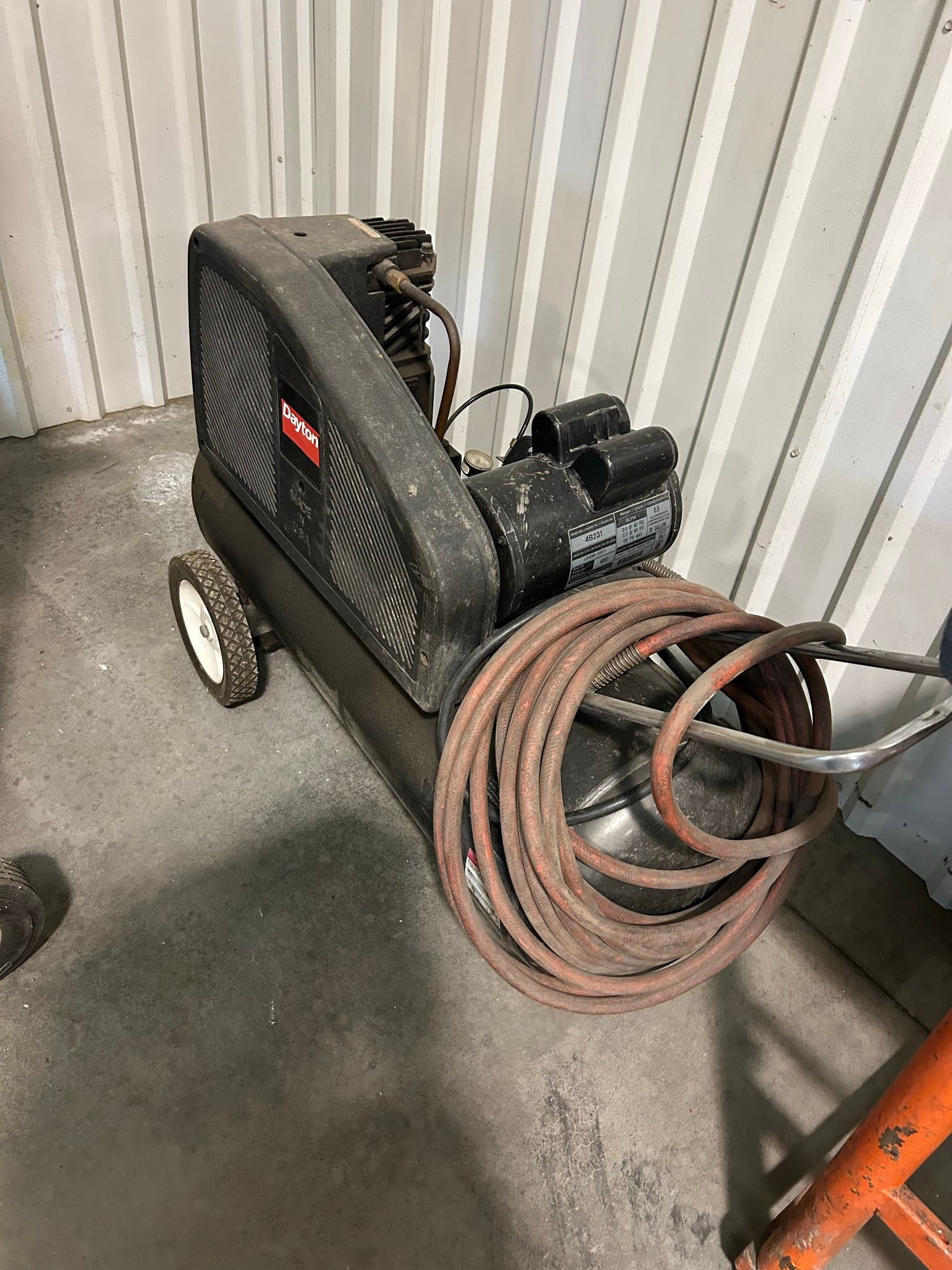 An air compressor with a hose attached to it is sitting on the floor in a room.