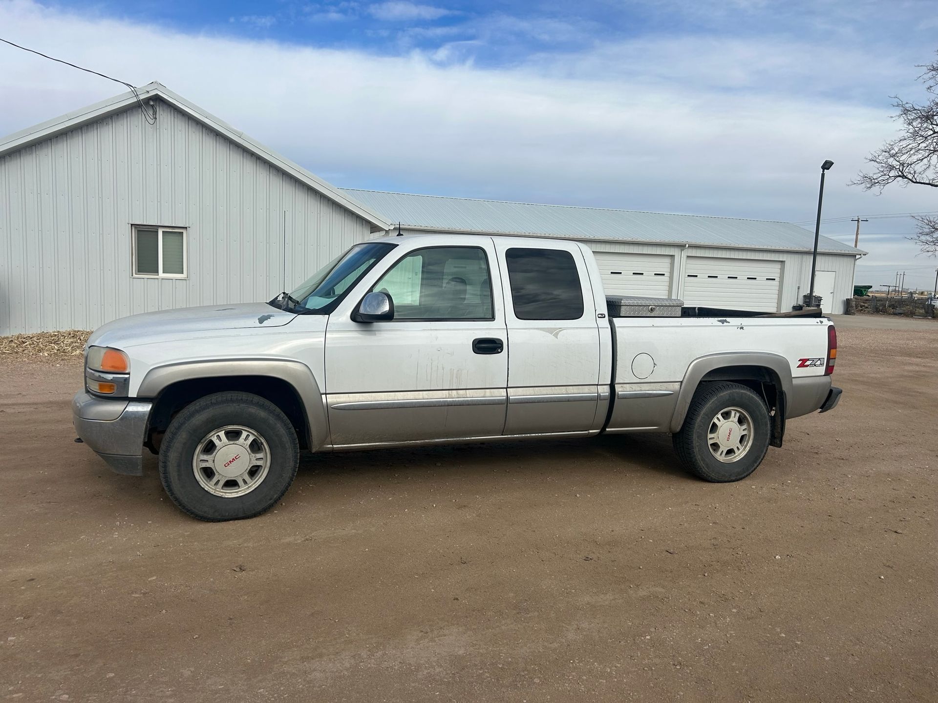A white truck is parked in a dirt lot in front of a building.