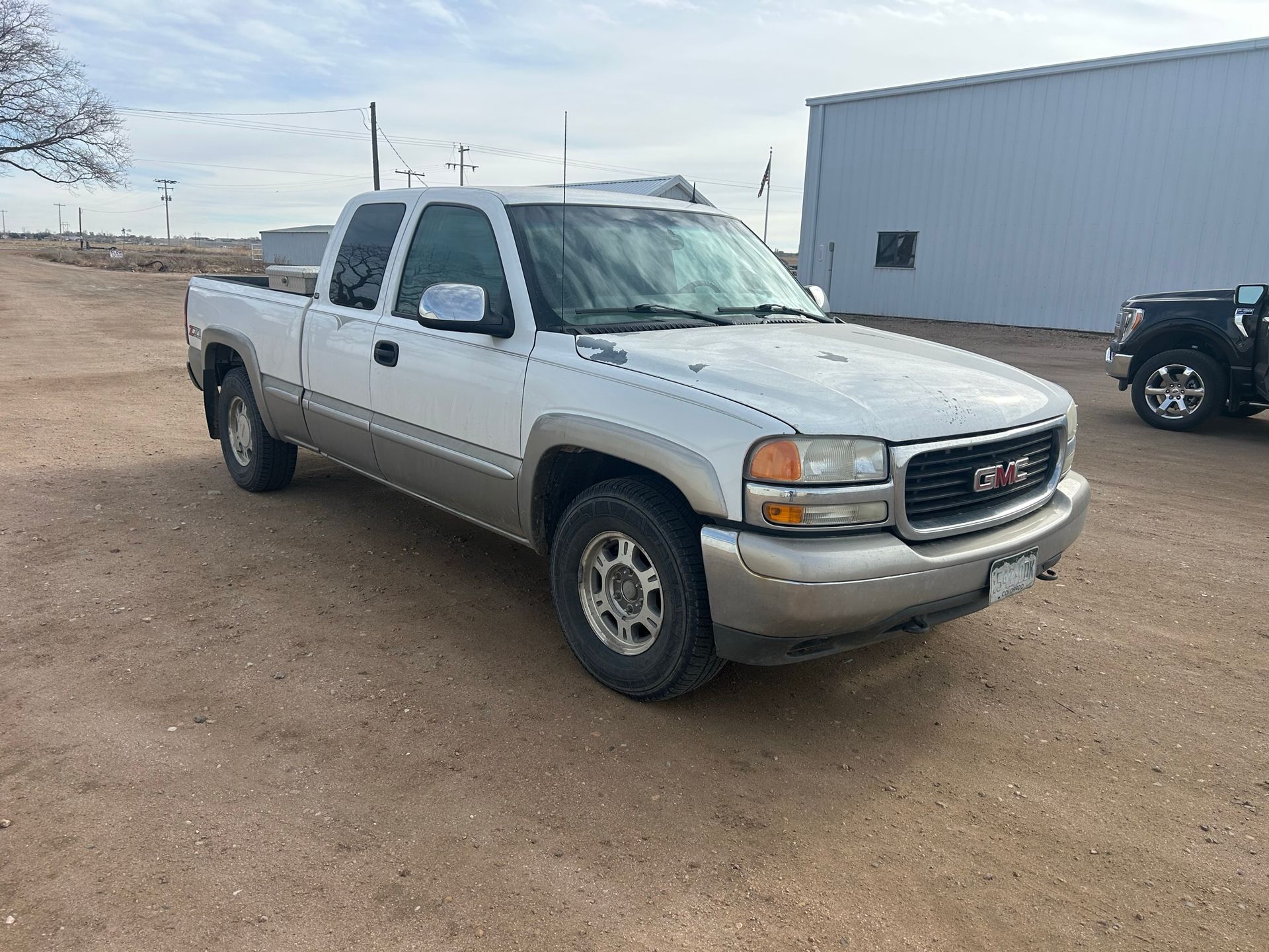 A white gmc truck is parked in a dirt lot in front of a building.