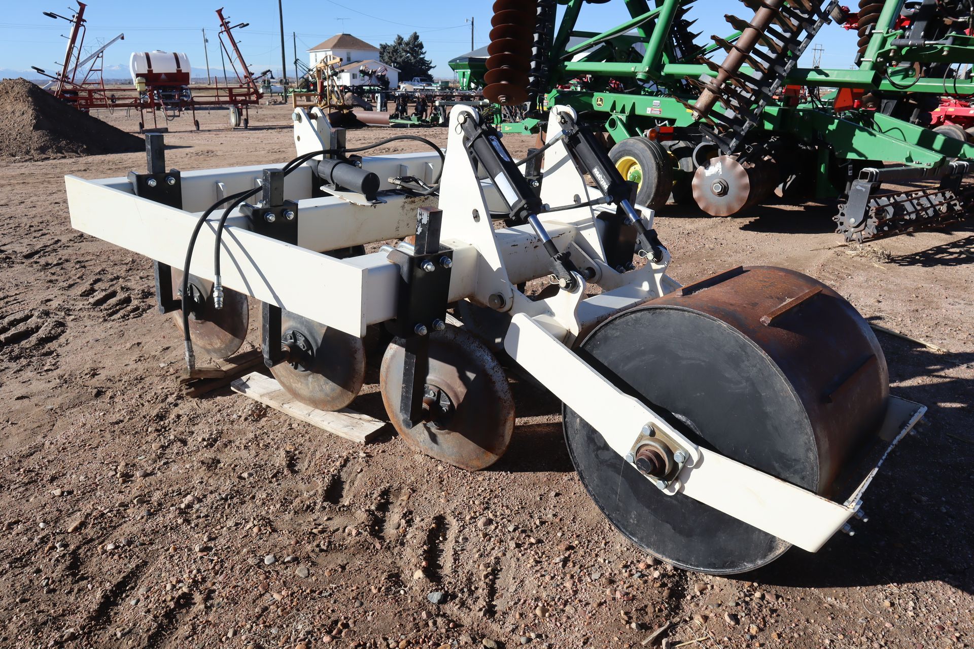 A tractor is parked in a dirt field with a large roller attached to it