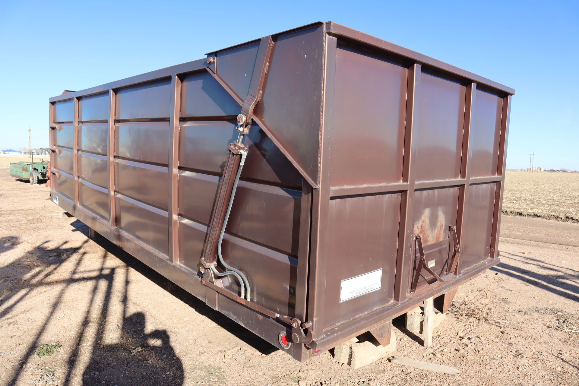 A large brown dumpster is sitting in a dirt field