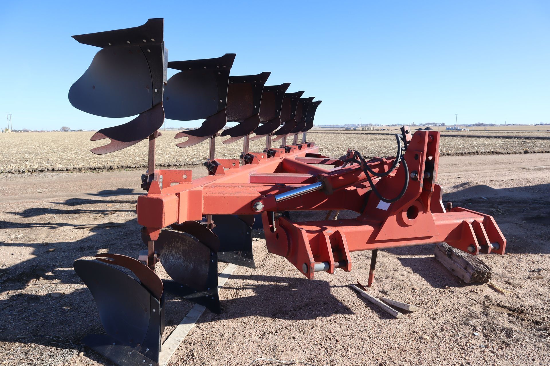 A red plow is sitting in a dirt field