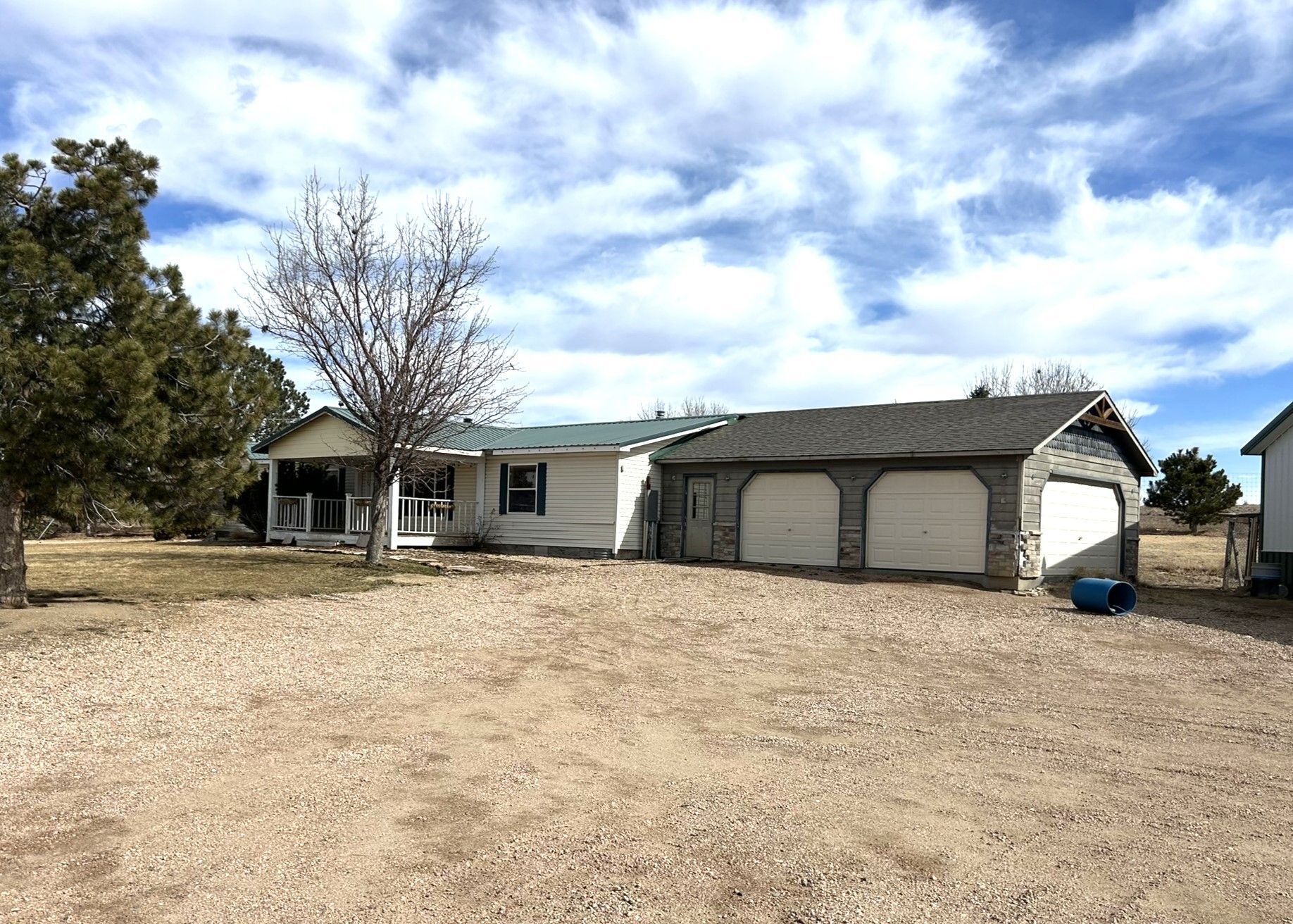A house with a garage and a porch in the middle of a dirt field.