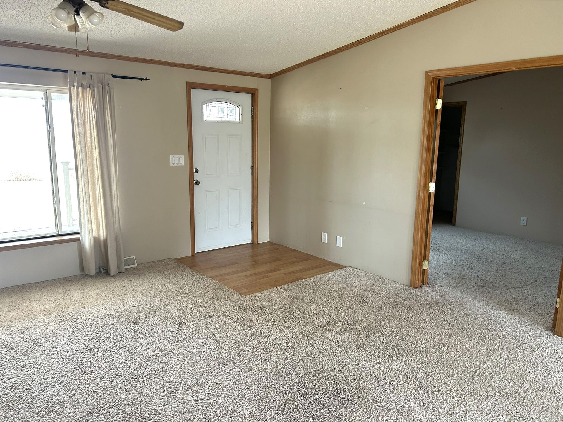 An empty living room with a ceiling fan and a door.