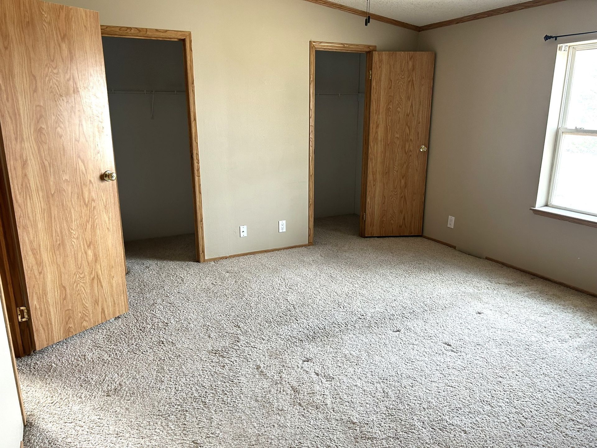 An empty bedroom with a carpeted floor and wooden doors.