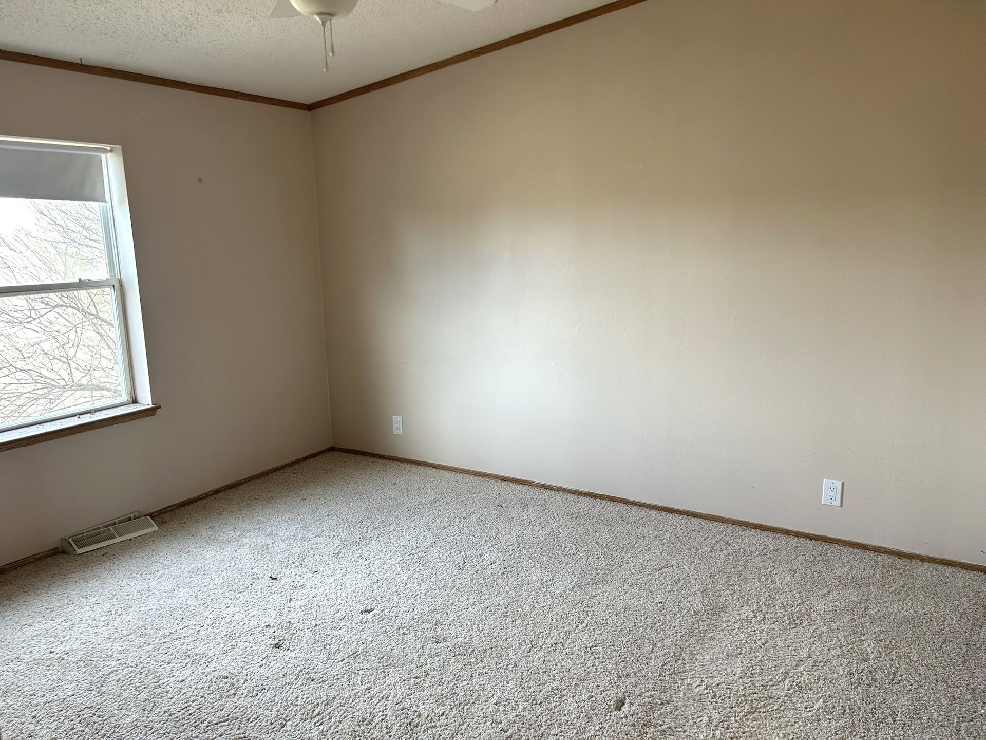An empty bedroom with a window and a ceiling fan.