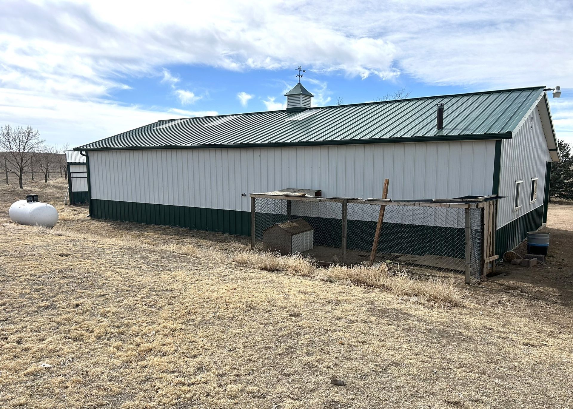 A white barn with a green roof is sitting in the middle of a field.
