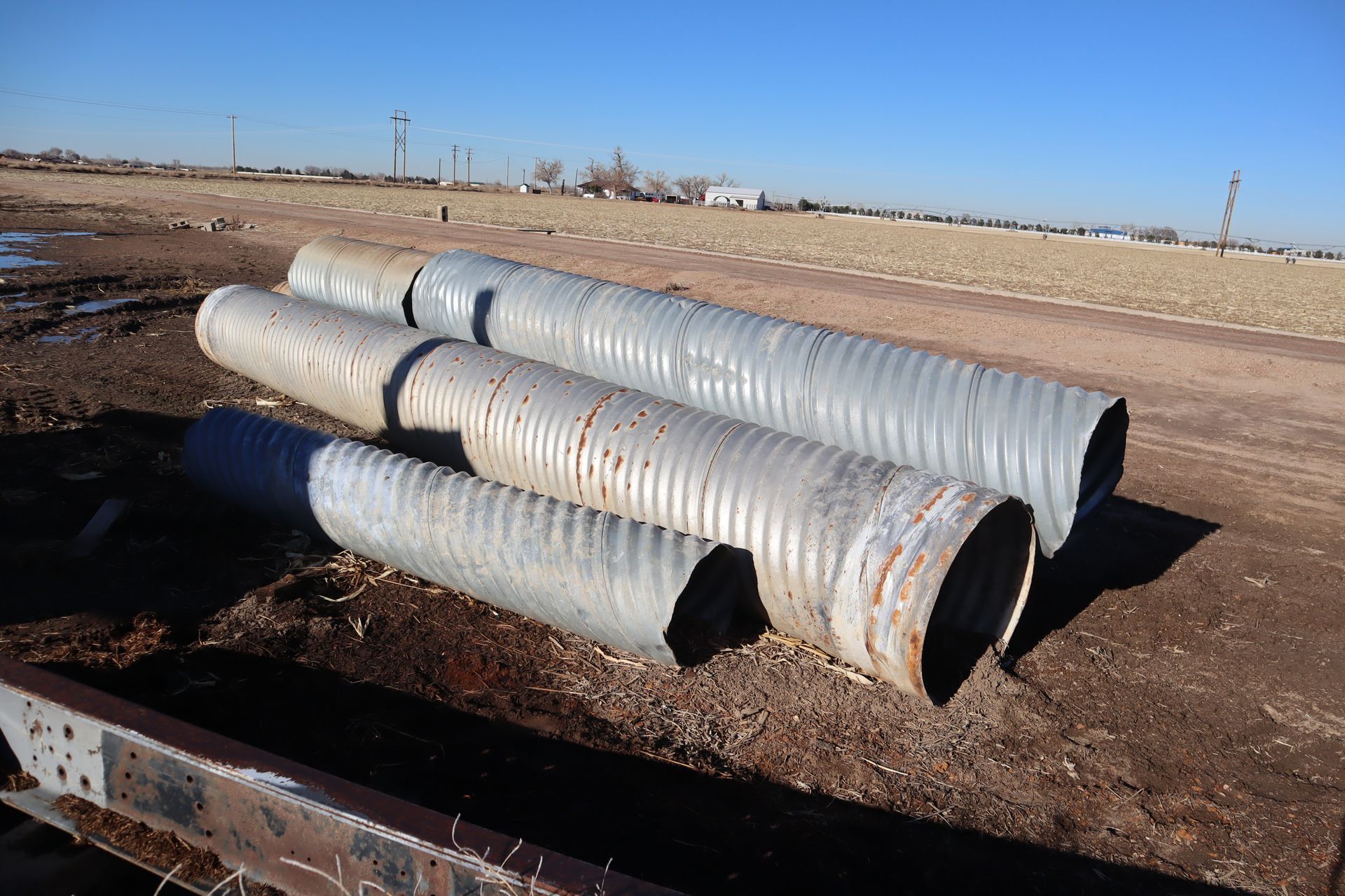 Three metal pipes are stacked on top of each other in a field