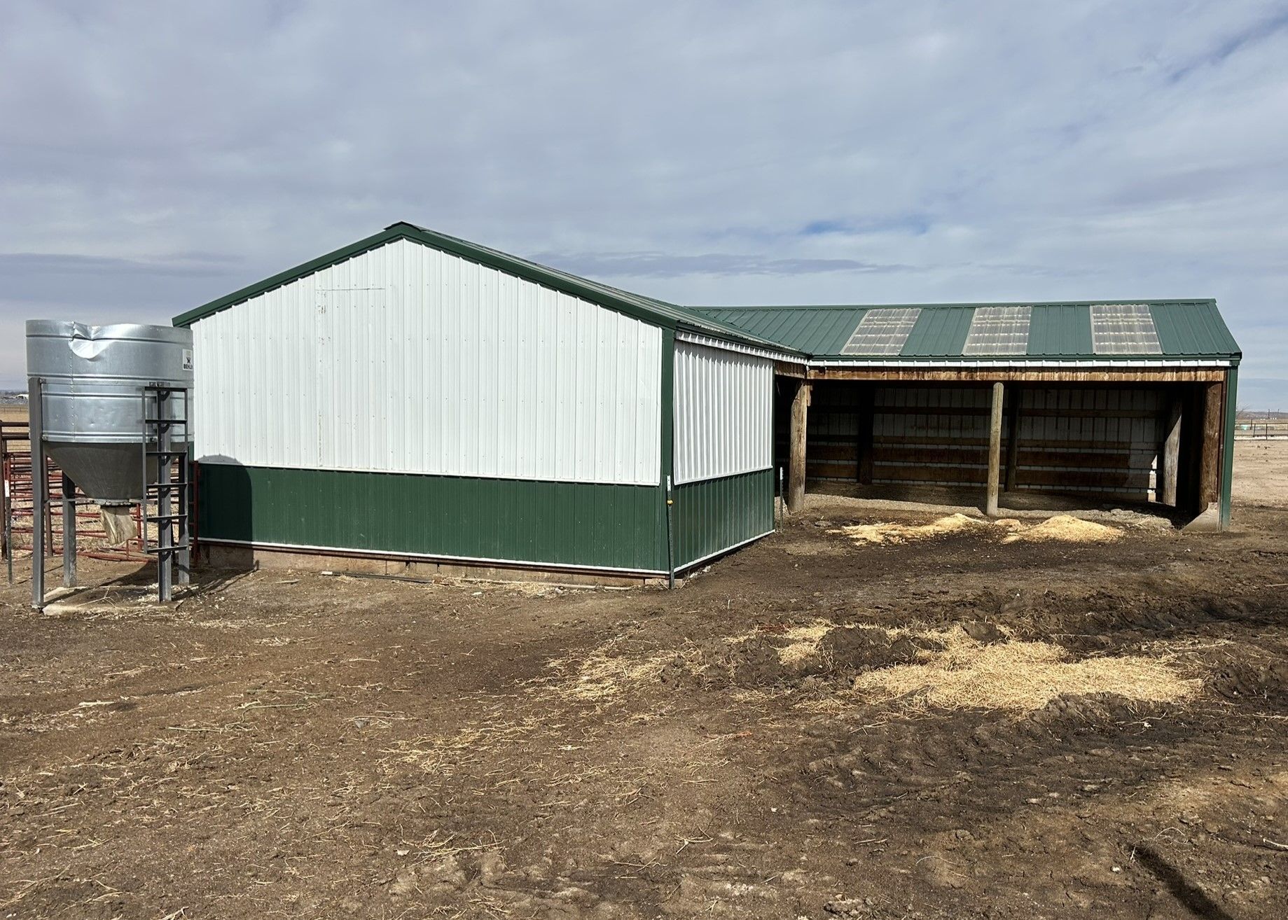 A white and green barn is sitting in the middle of a dirt field.