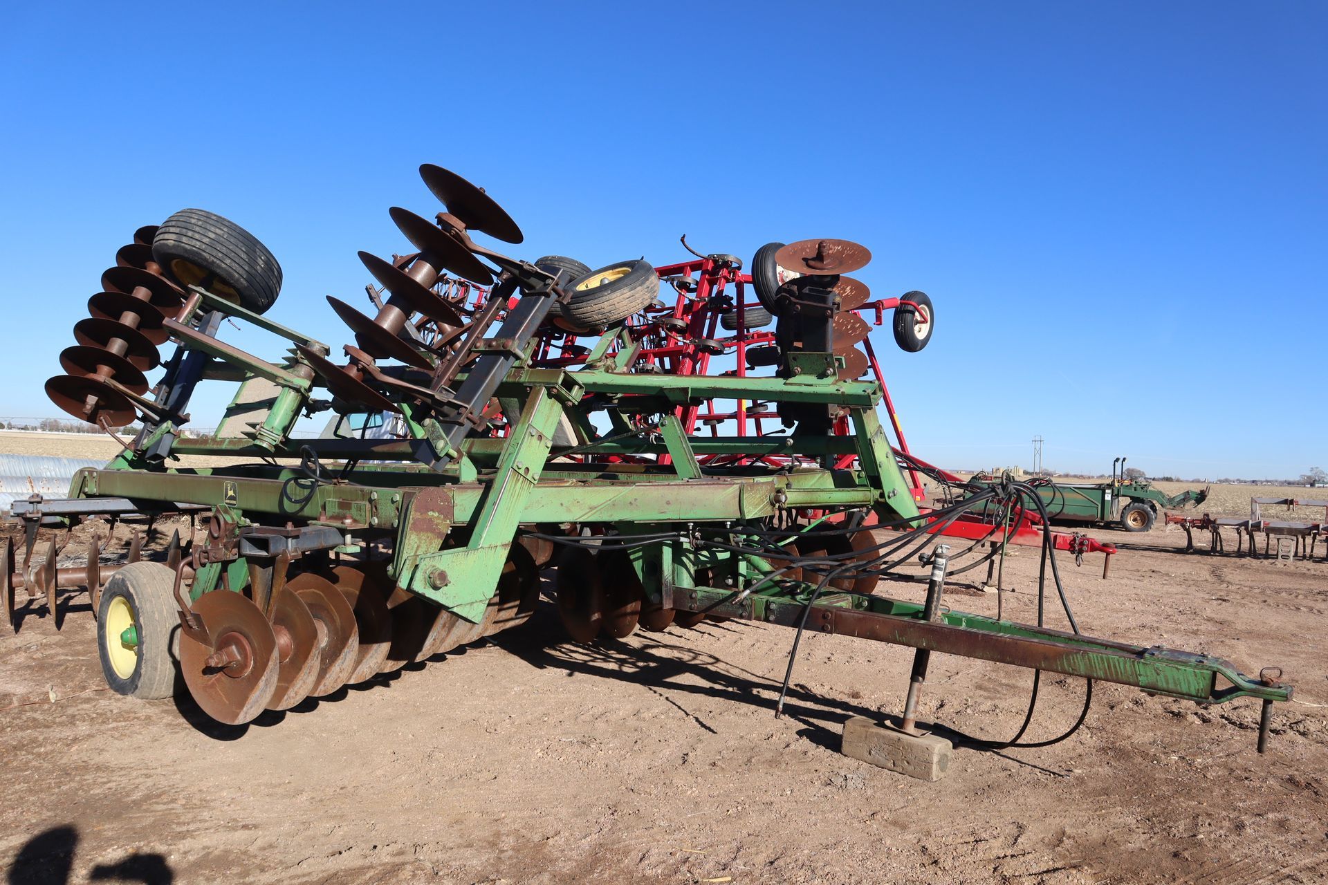 A green and red tractor is parked in a dirt field.