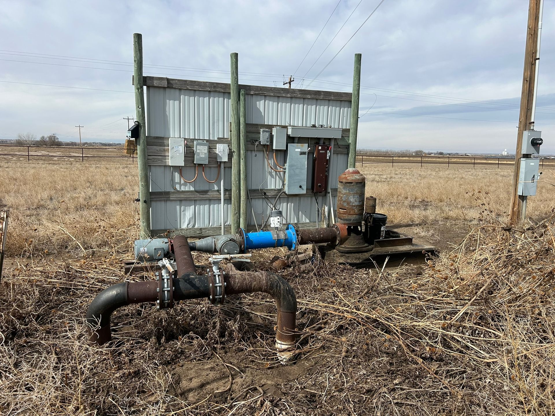 A water pump is sitting in the middle of a dry grass field.