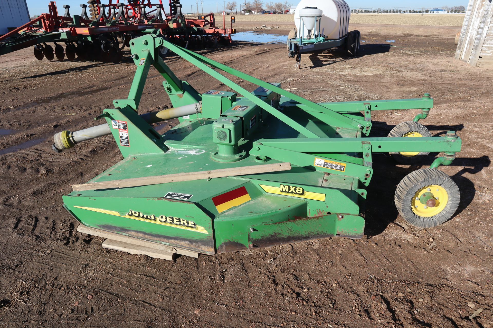 A green john deere lawn mower is parked in a dirt field