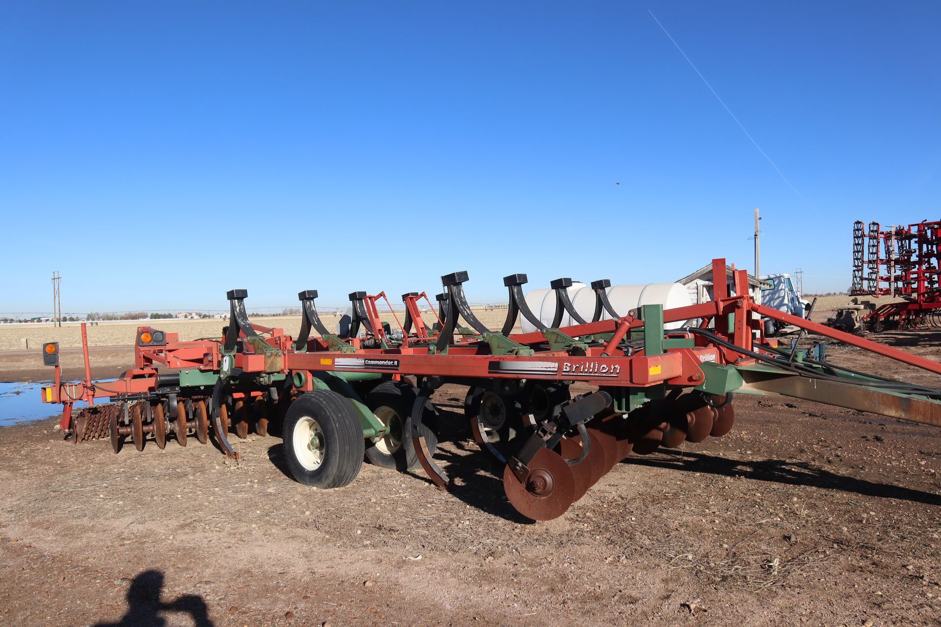 A red and green tractor is parked in a dirt field.