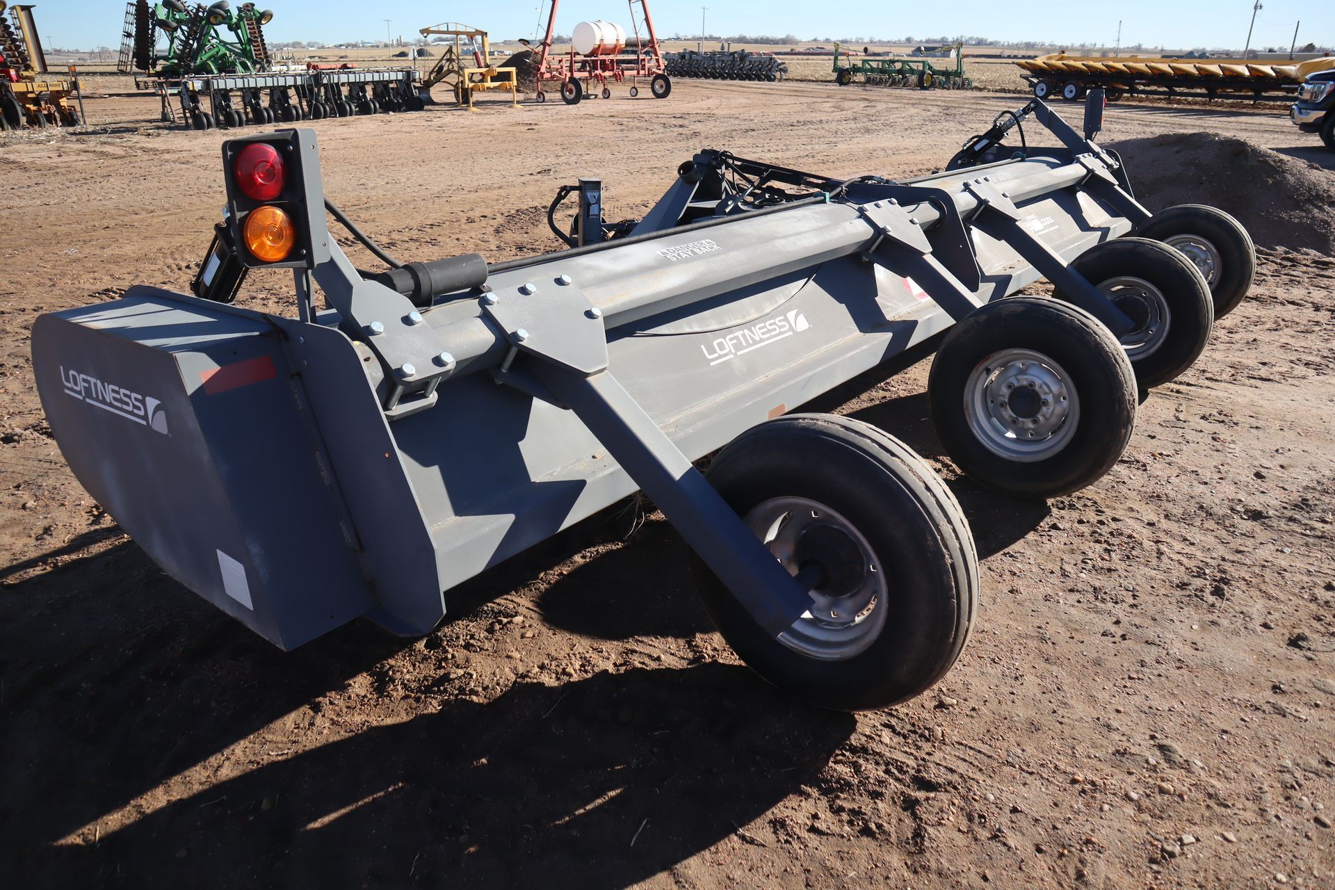 A row of tractors are parked in a dirt field
