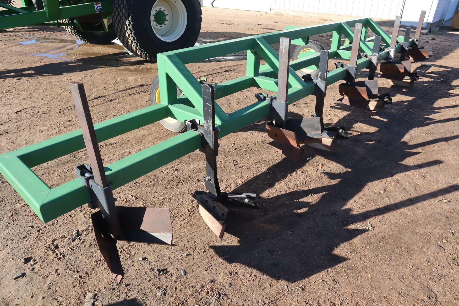 A green tractor is parked in the dirt next to a green frame