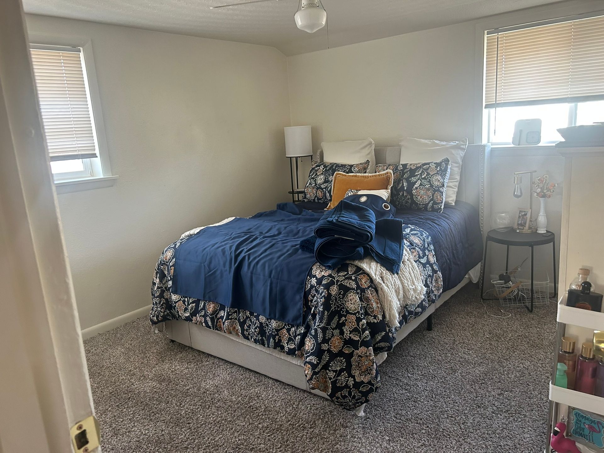 A bedroom with a bed , nightstand , lamp and window.