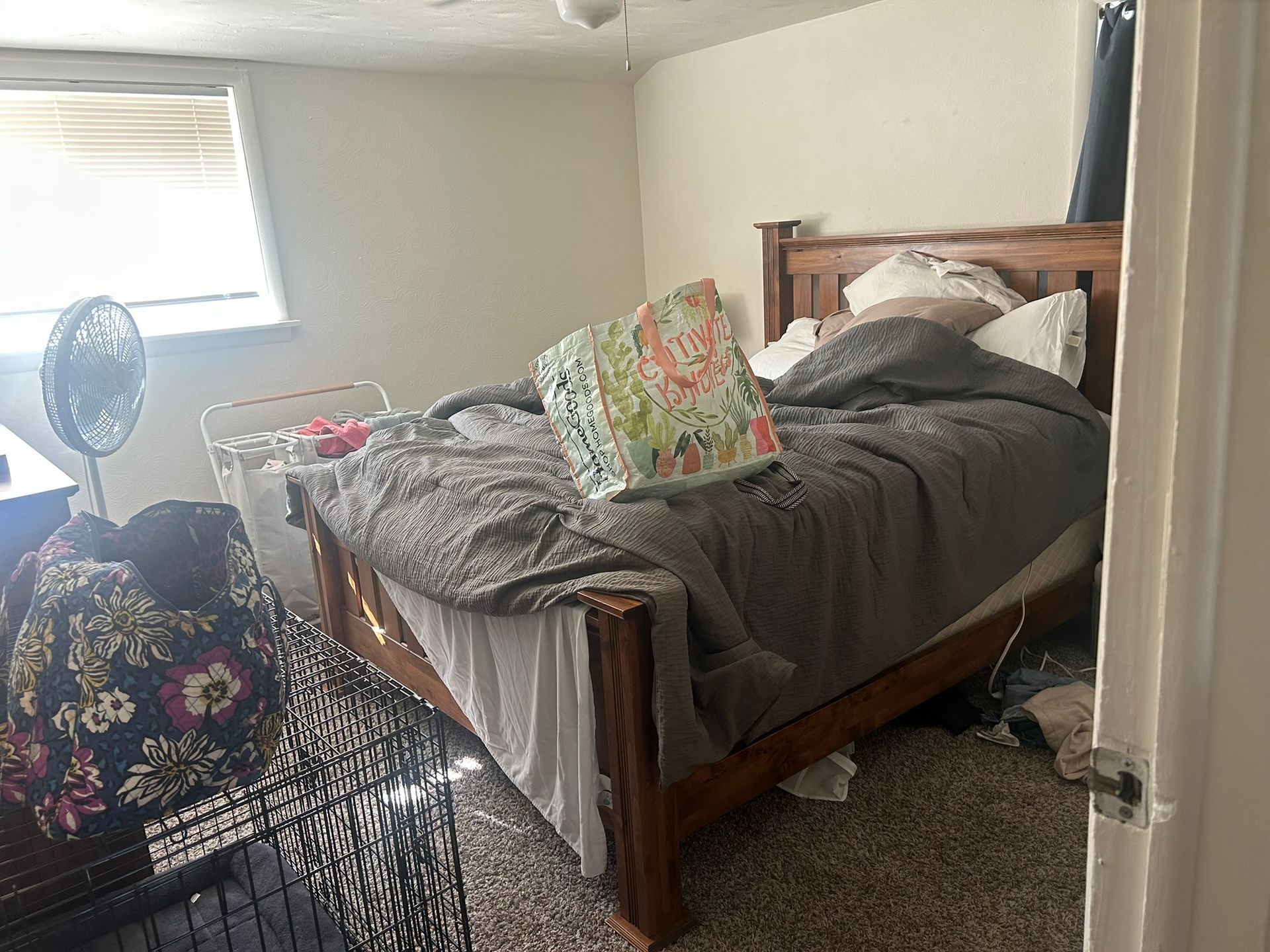 A bedroom with a bed , a fan , and a cage.