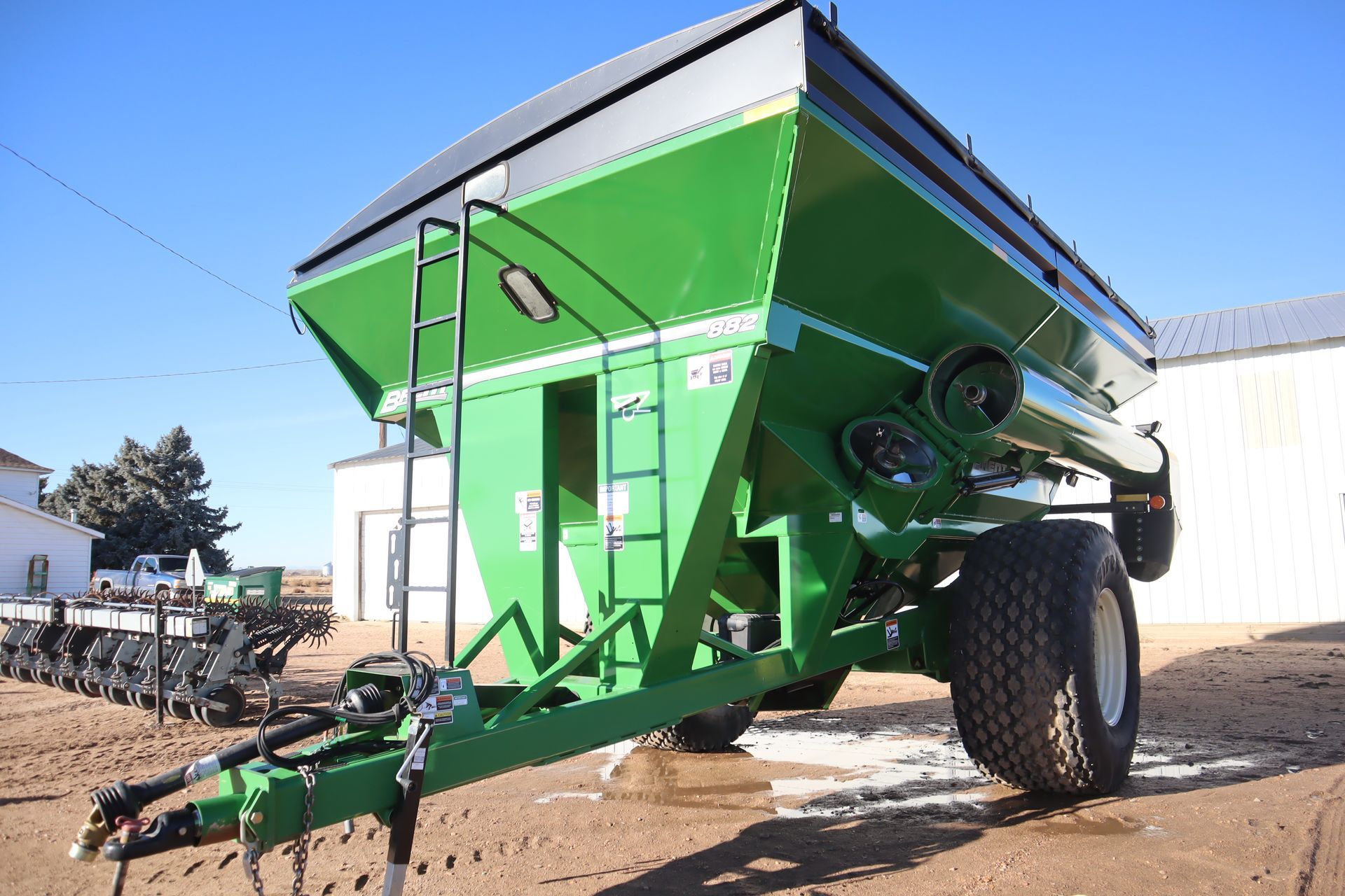 A green trailer with a ladder attached to it is parked in front of a building.