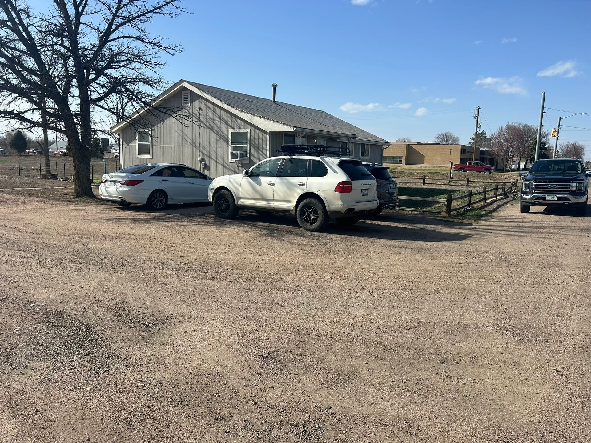 Three cars are parked in a gravel lot in front of a house.