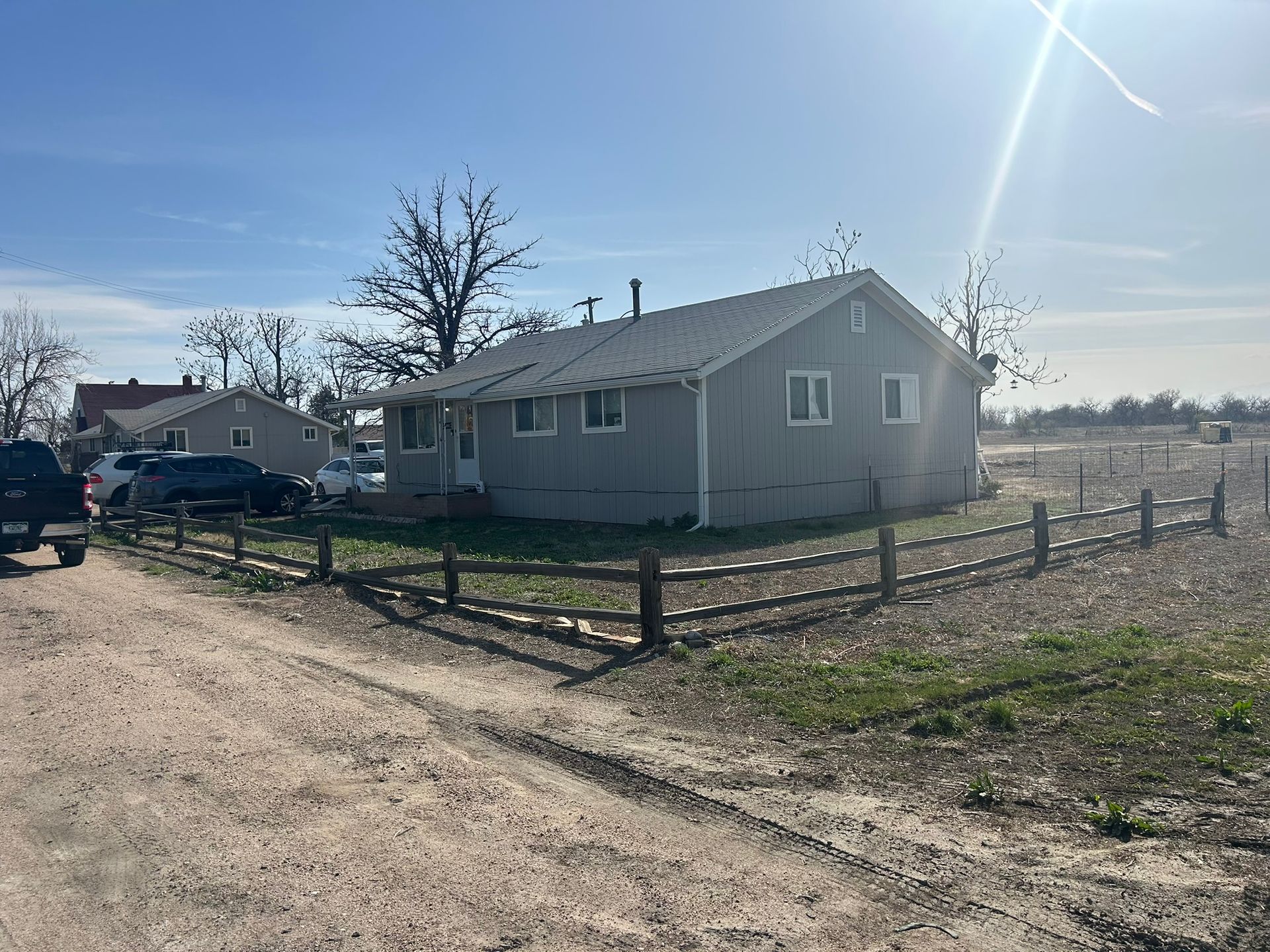A house is sitting in the middle of a dirt road next to a wooden fence.