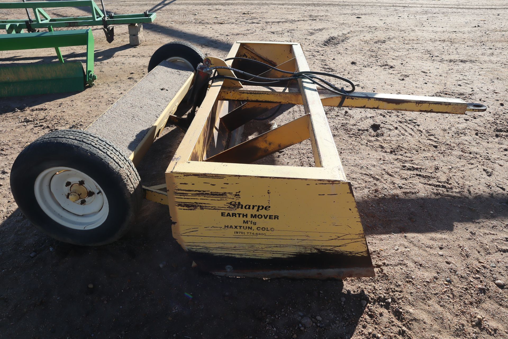 A yellow sharpe tractor sits on a dirt field